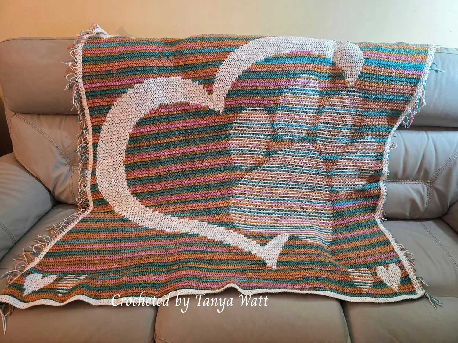 Crocheted mosaic afghan draped over a couch, featuring a large white heart outline with a paw print inside