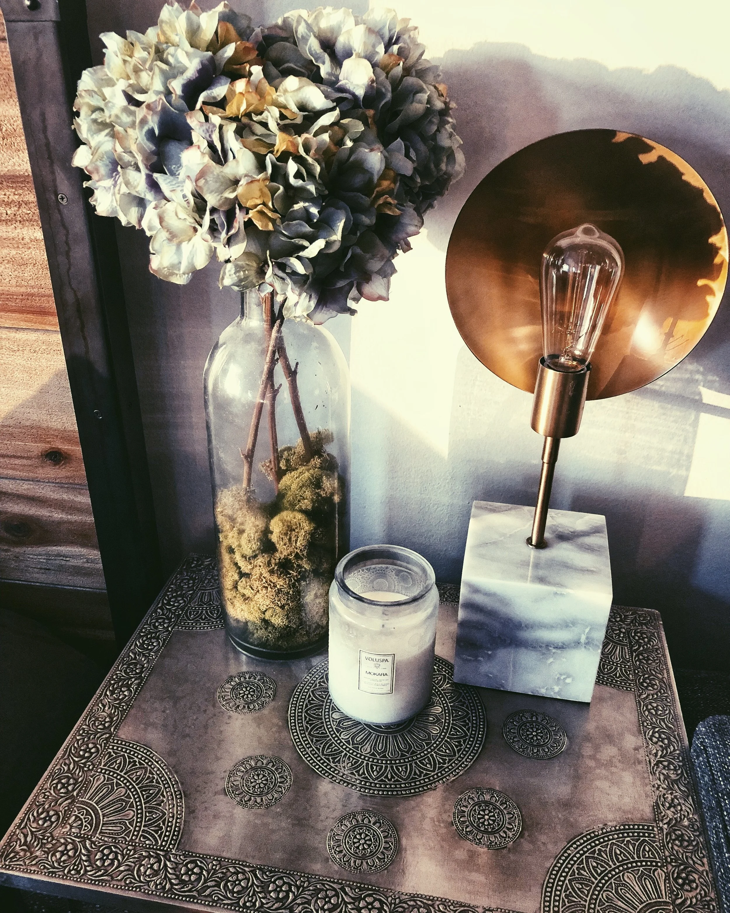 Rustic home decor bedside table with faux flowers, home fragrance, and Edison bulb lamp.