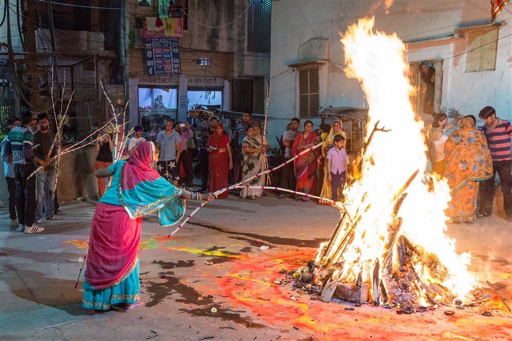 Lady throwing painted bamboo sticks in Holi bonfire