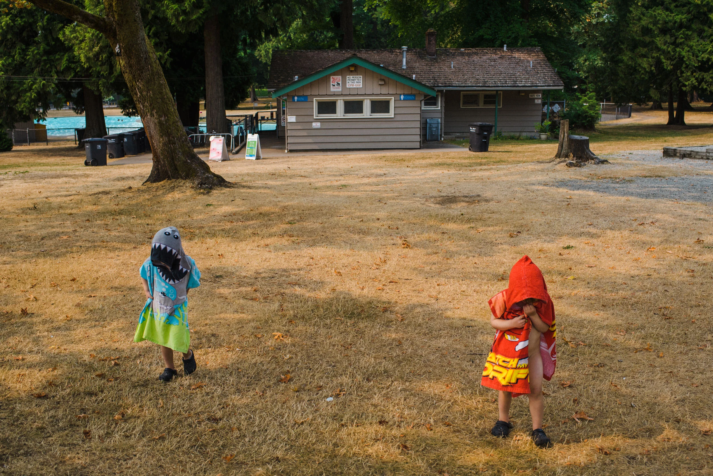 Twin boys walking in the park dressed in pool towels.