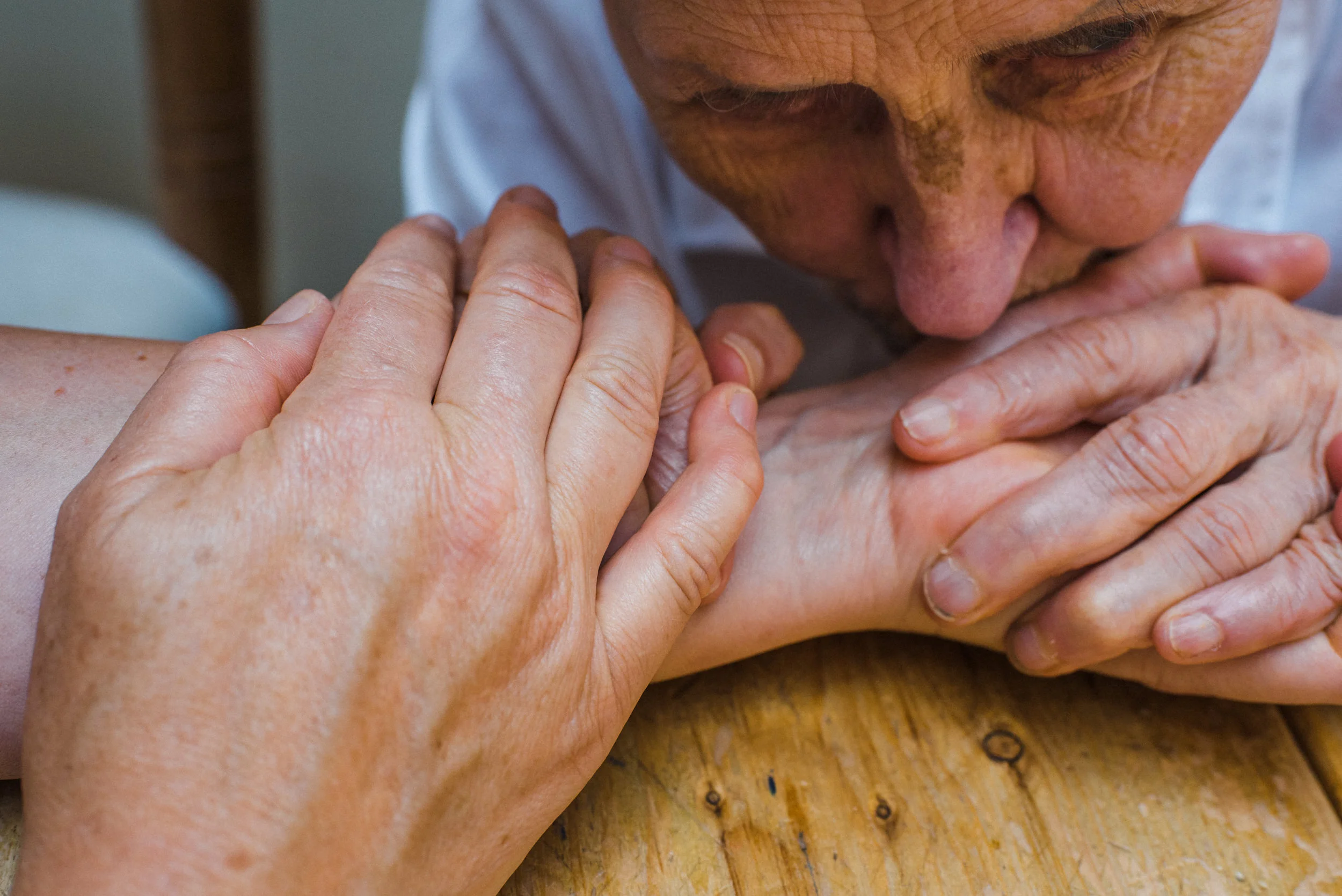An elderly woman kisses her daughter’s hand.