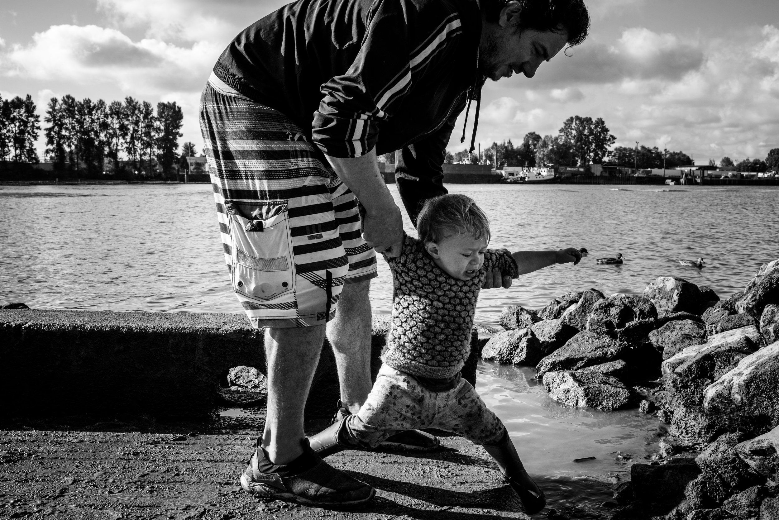 Dad catching his toddler boy from falling into the water by the river.