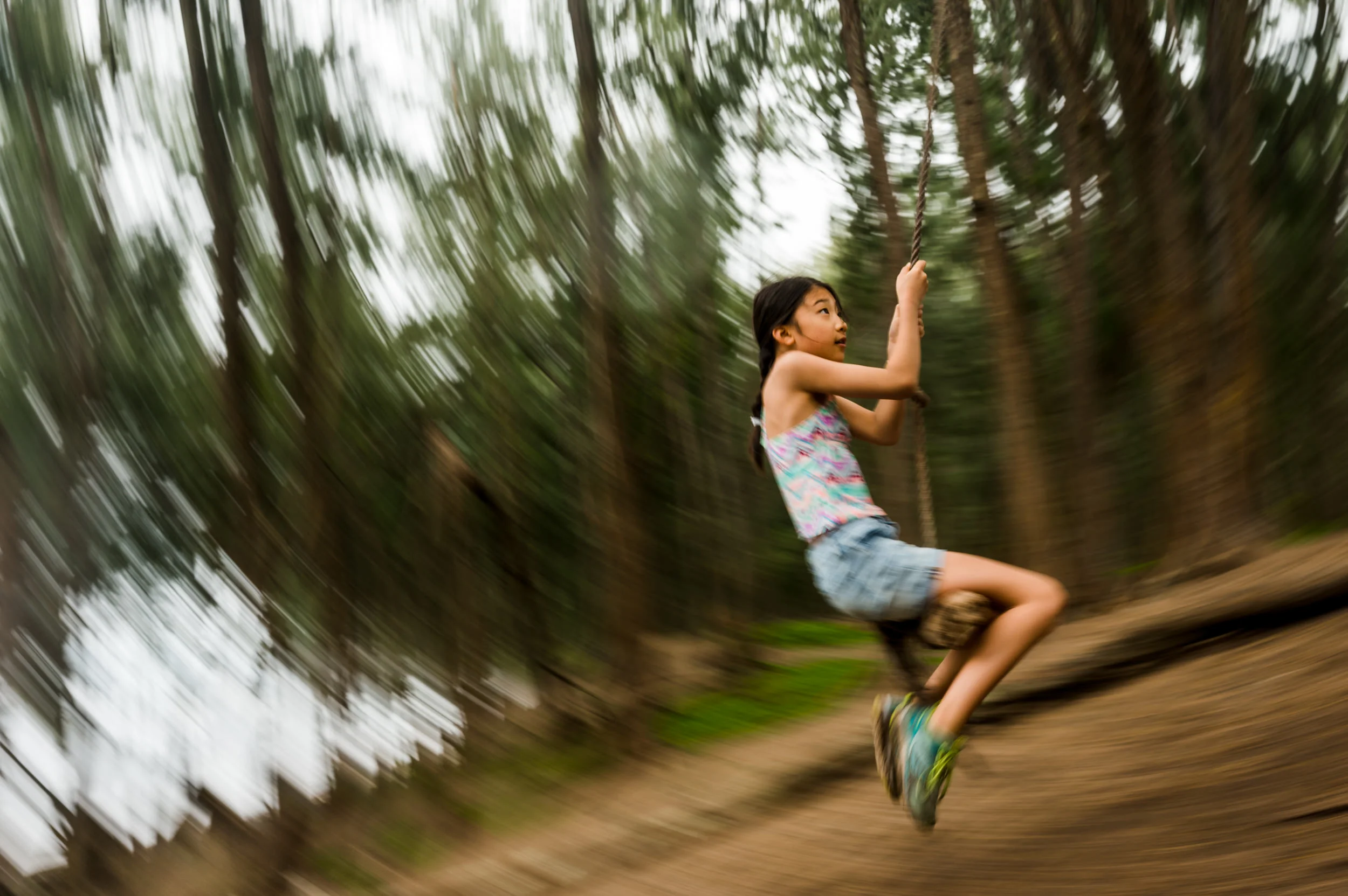 Family Vacation photographer. Girl swinging from a tree rope in the forest.