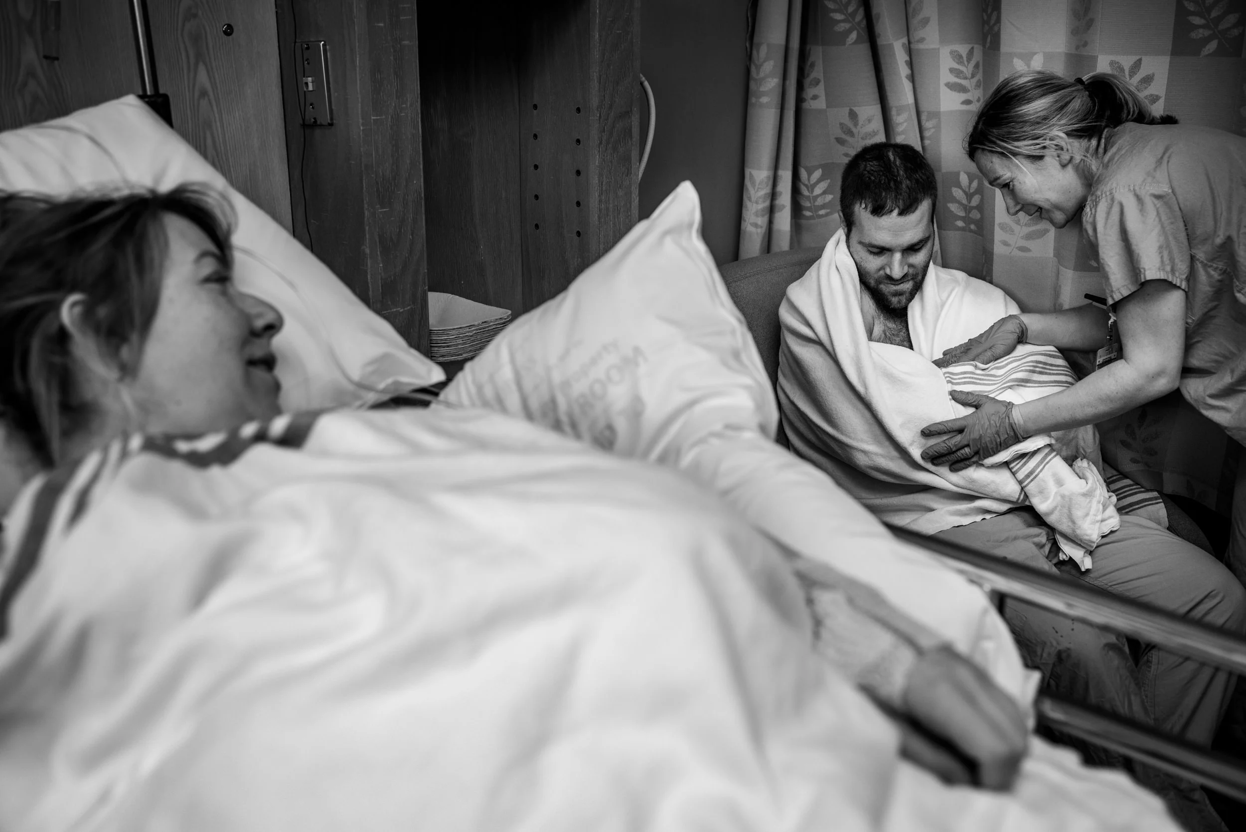 Mother looking at father who is holding their first newborn baby girl, North Vancouver Lions Gate Hospital.