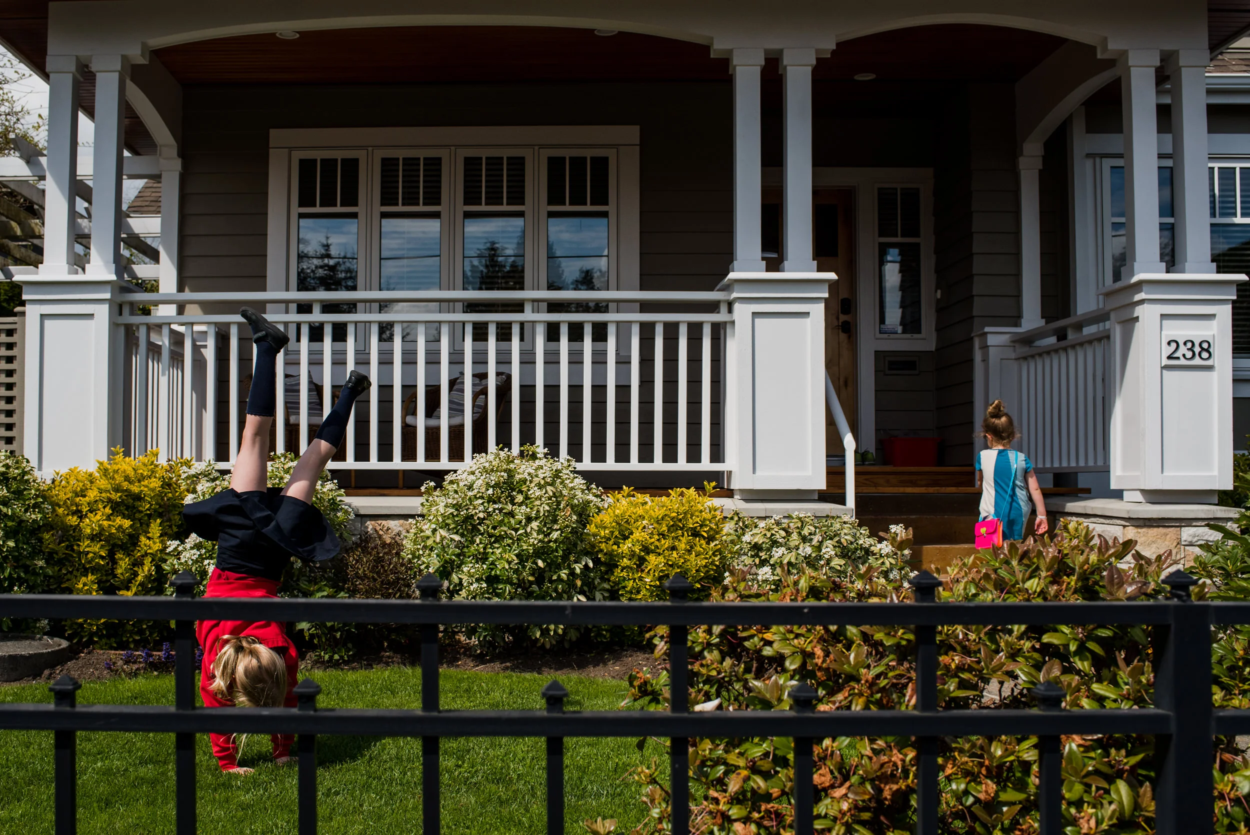 Day in the life of families. Girl doing cartwheels in the front yard of her house while her sister walks inside.