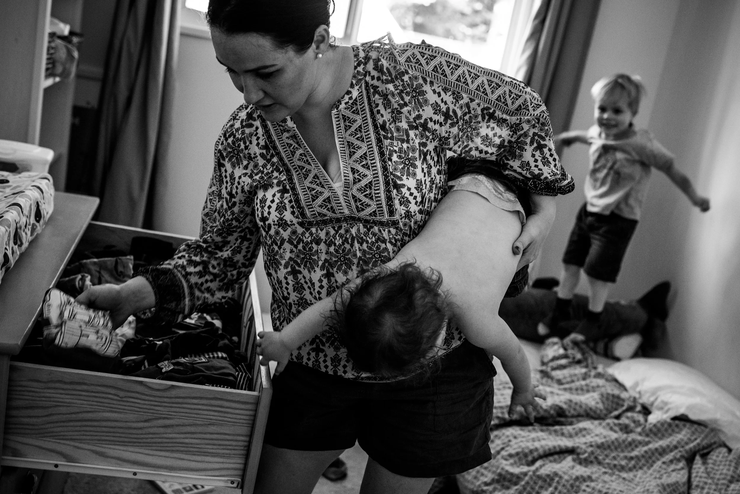 Day in the life of families. mom getting her sons dressed for the day while they are playing around in the room.