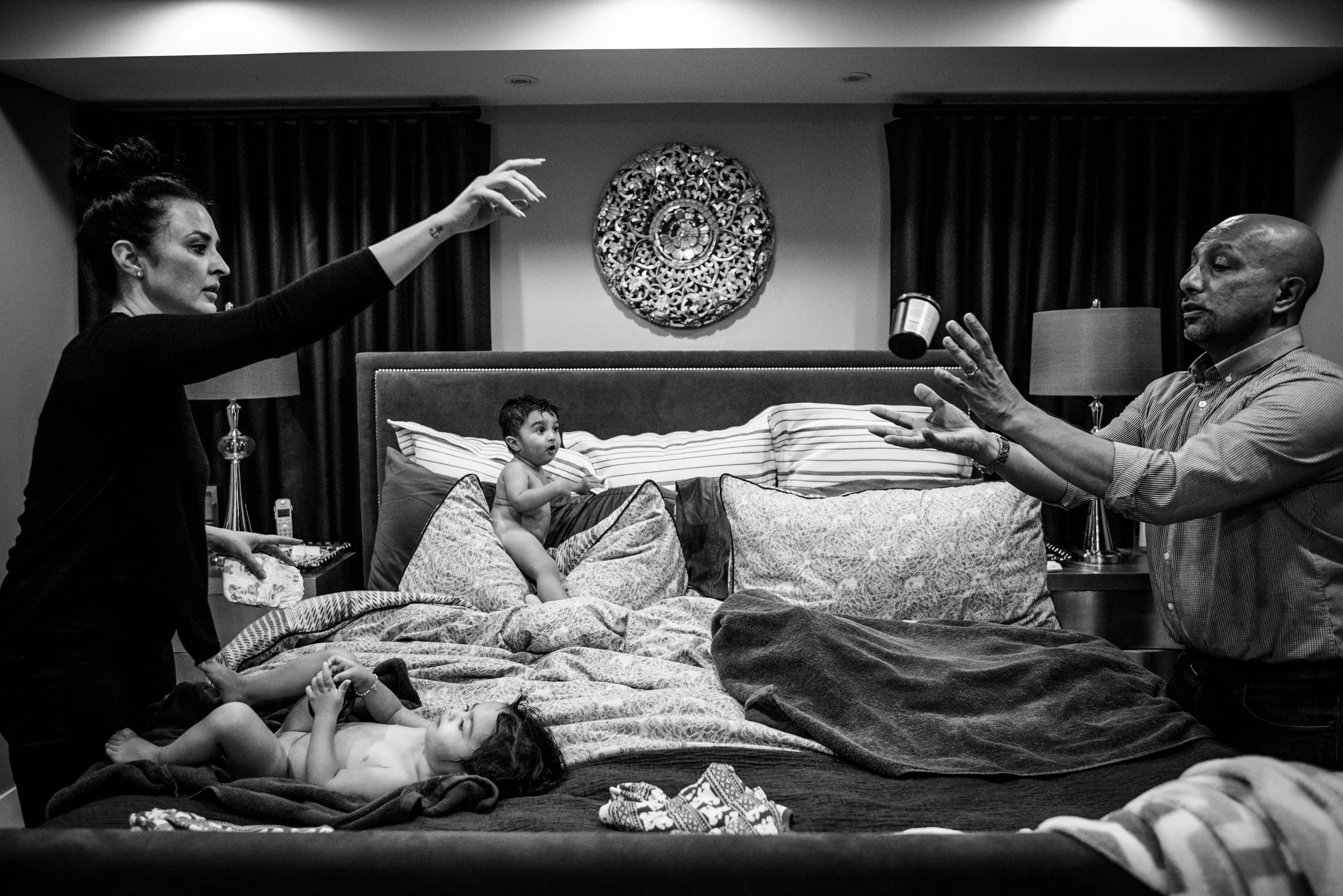 Best family photographs. Mom tossing diaper cream over to dad while naked twins are playing on the bed.
