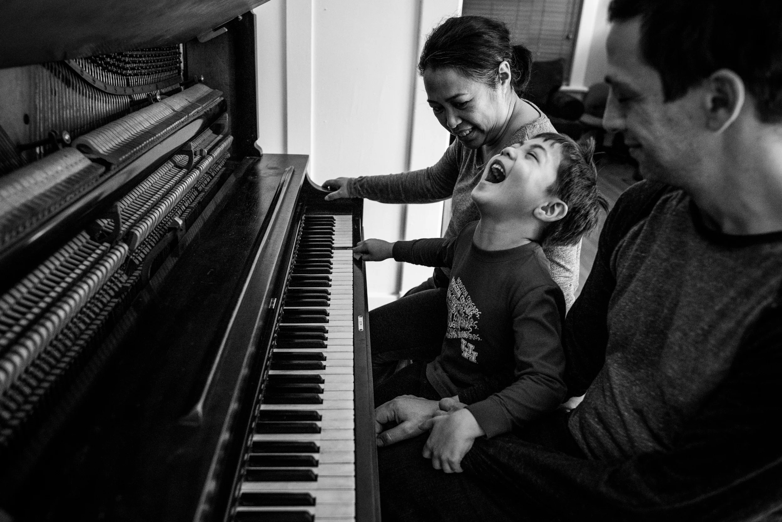 Day in the Life Family. Mom and dad laughing with son while playing music together on the piano.