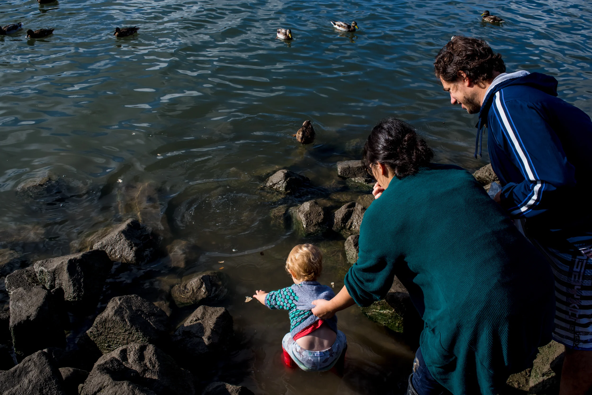 Day in the life of families. Mom holding on to her toddler boy's shirt so he doesn't fall into the water.