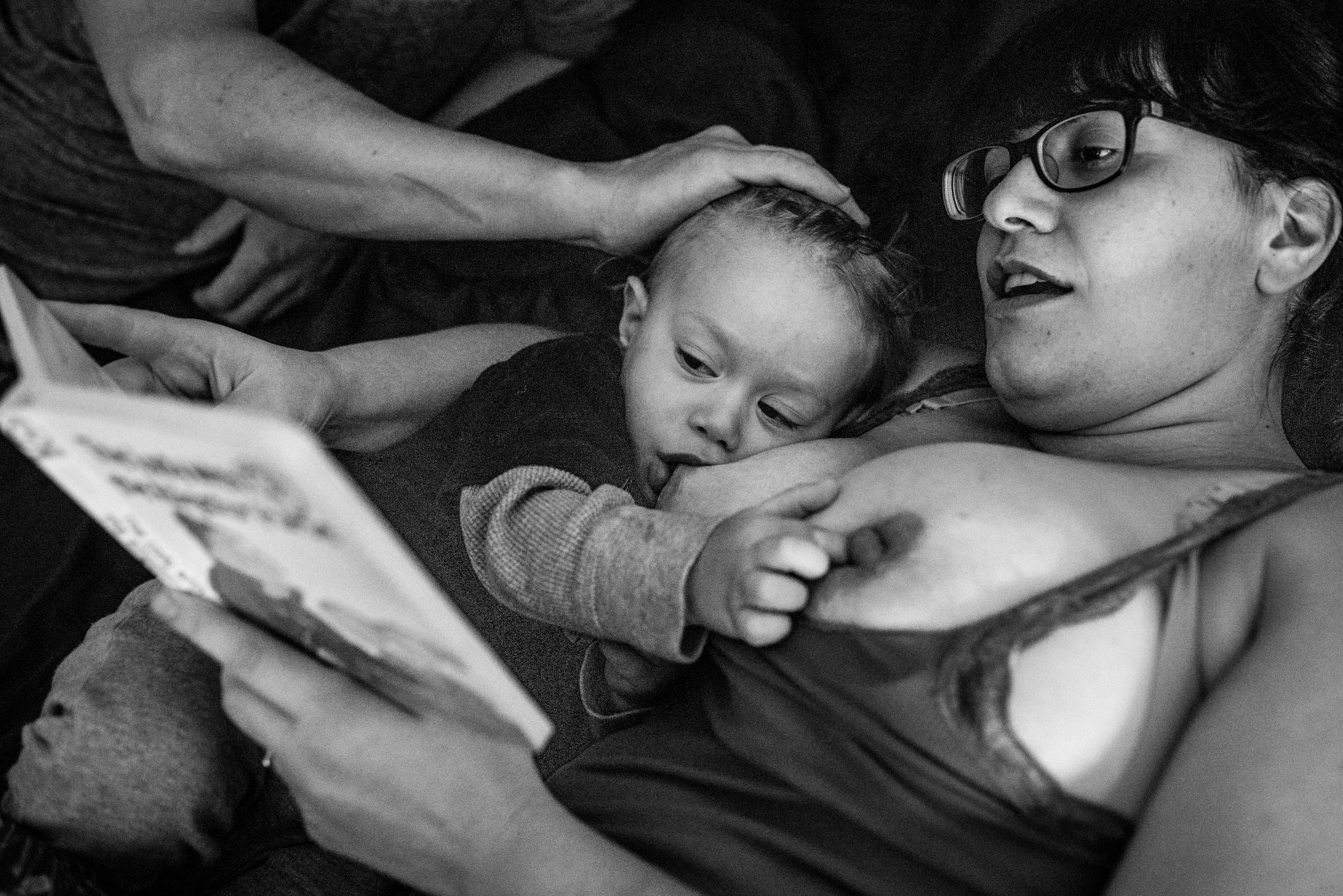 Day in the life with a baby. Boy breastfeeding while mom reads a book to him.
