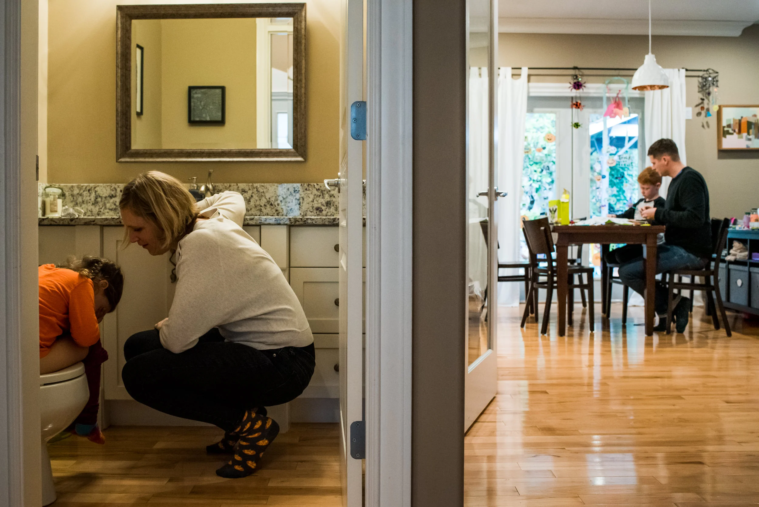 Day in the Life of Family. Father plays games with son at kitchen table and mom is with daughter in the washroom.