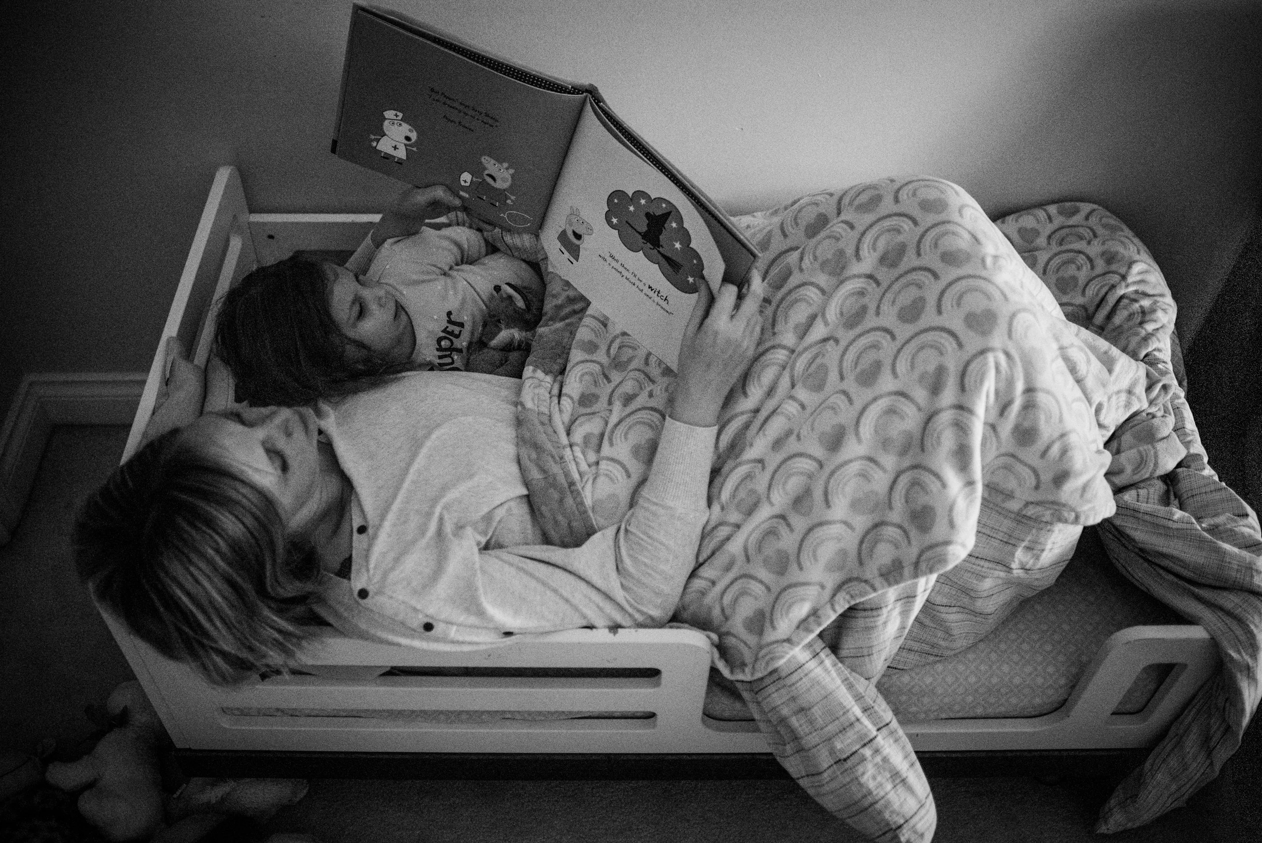 Awesome family photos. Mom lying in toddler bed with her daughter reading before bedtime.