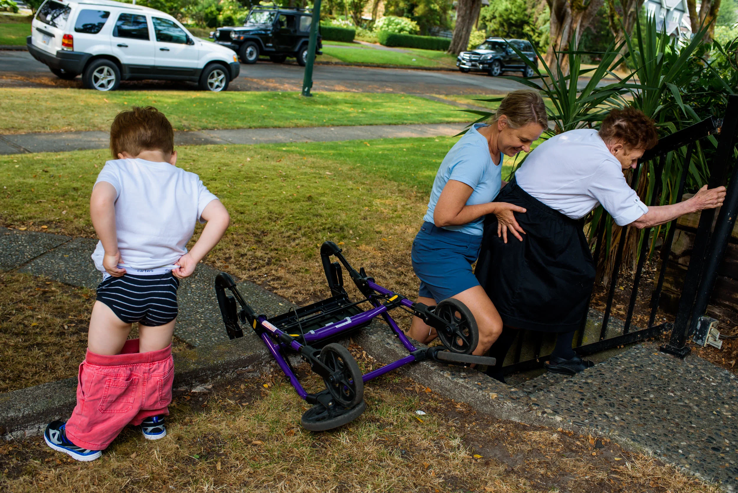 Day in the Life Family. Mom helping grandmother up the steps to the house while her son pees onto the front yard.