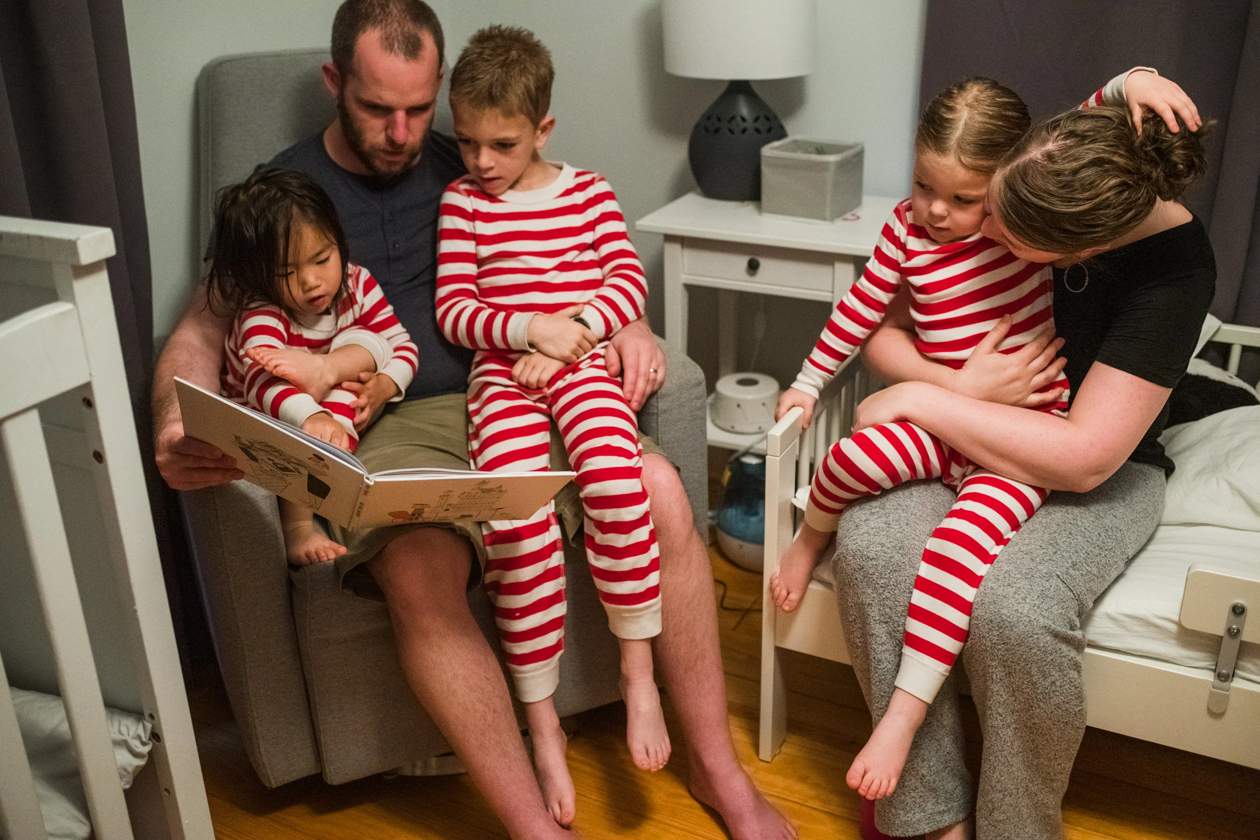 Parents are cuddling with their three children while reading books before bed.