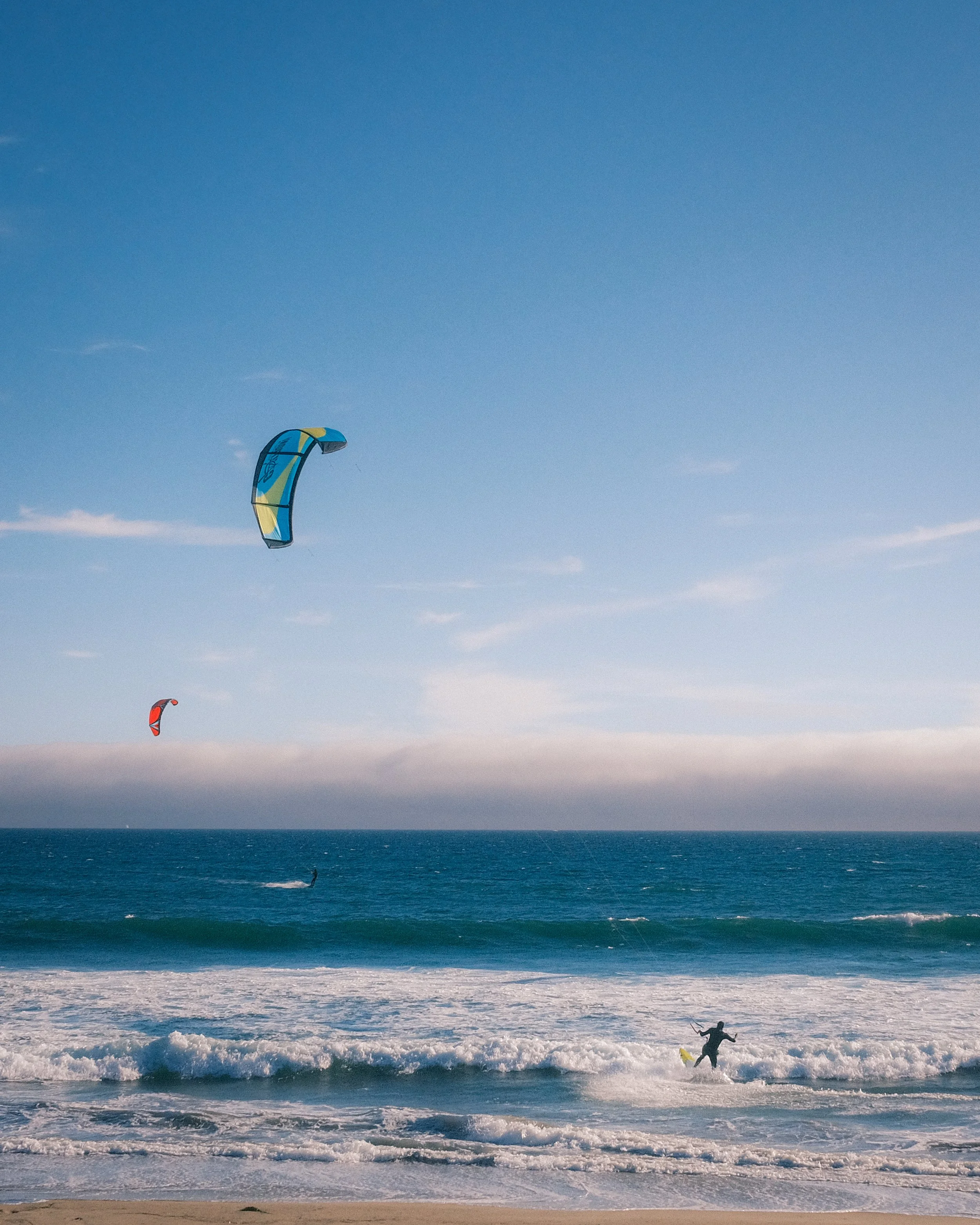 Kite surfers riding the waves on the ocean with colorful kites flying in the clear sky.