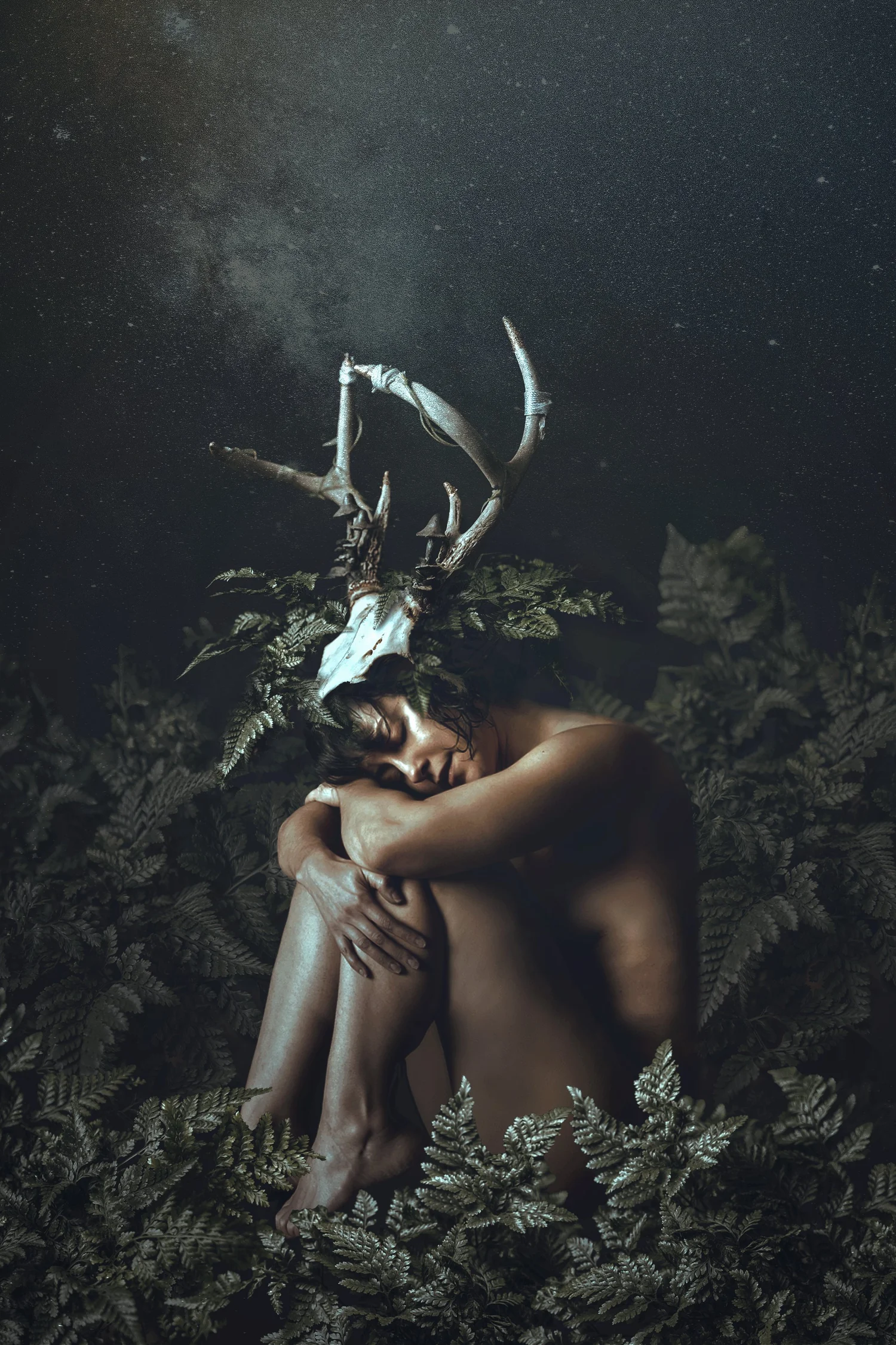 A seated figure wearing an antlered skull headdress among dark ferns