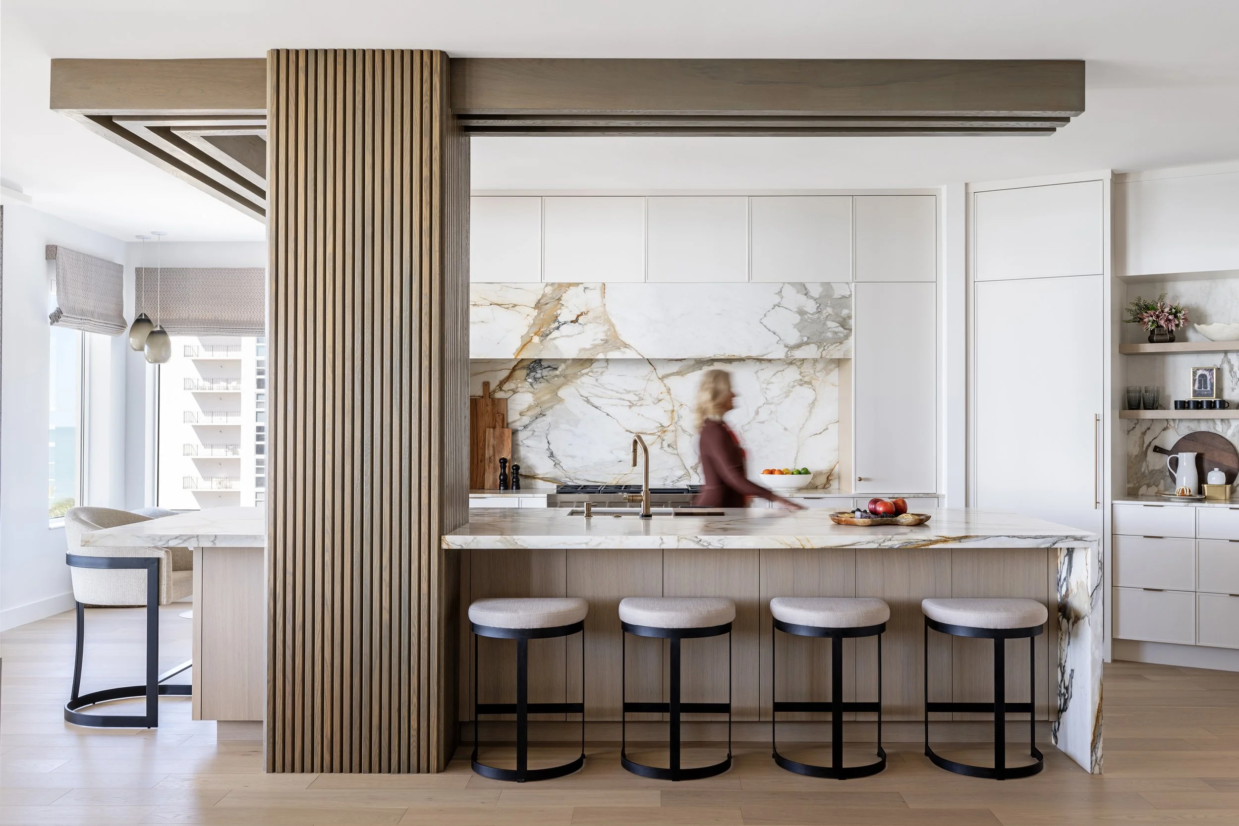 Kitchen with warm cabinets and calacatta macchia veccia marble countertops and backsplash with upholstered barstools