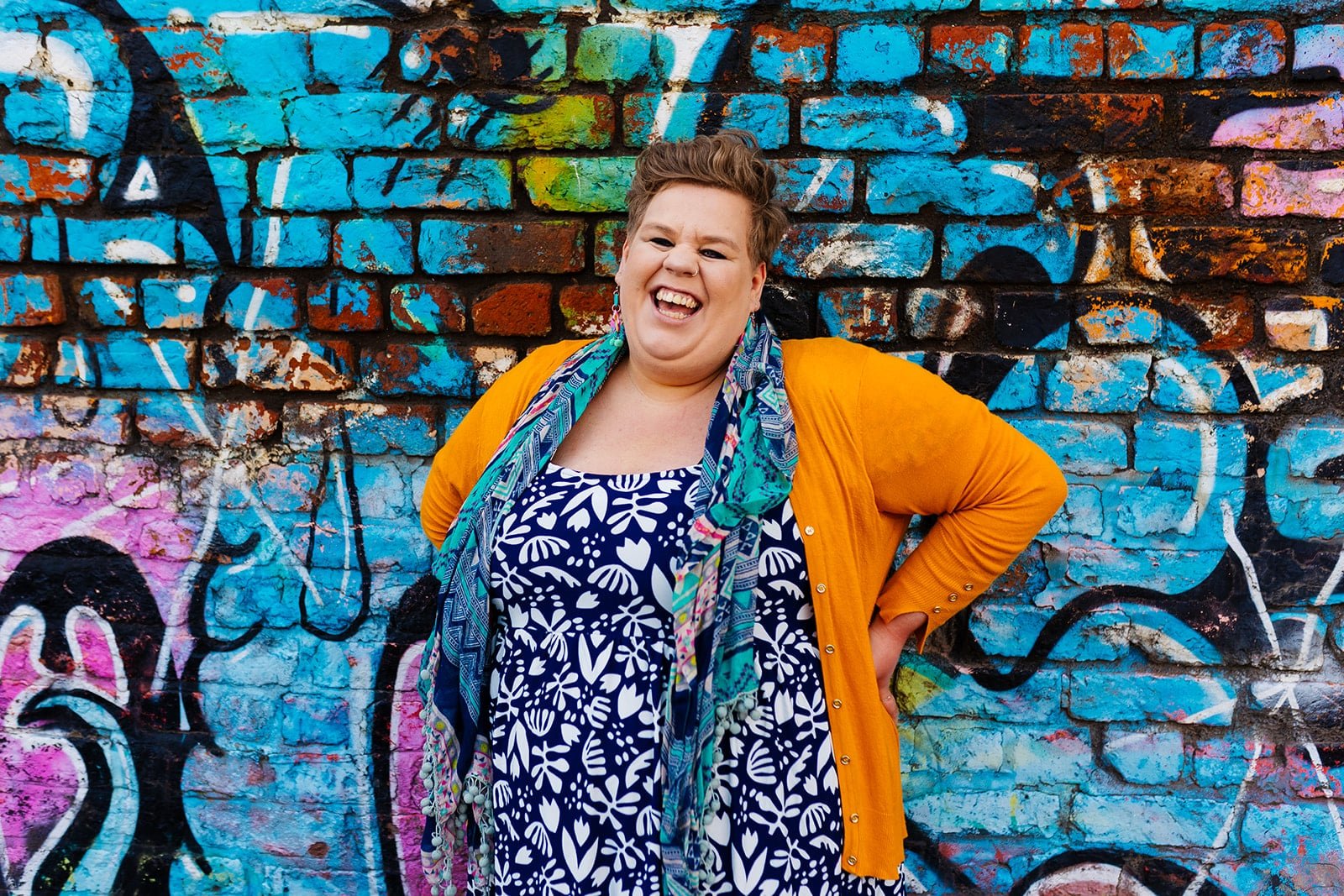 Meg laughing, stood next to a graffitied wall.