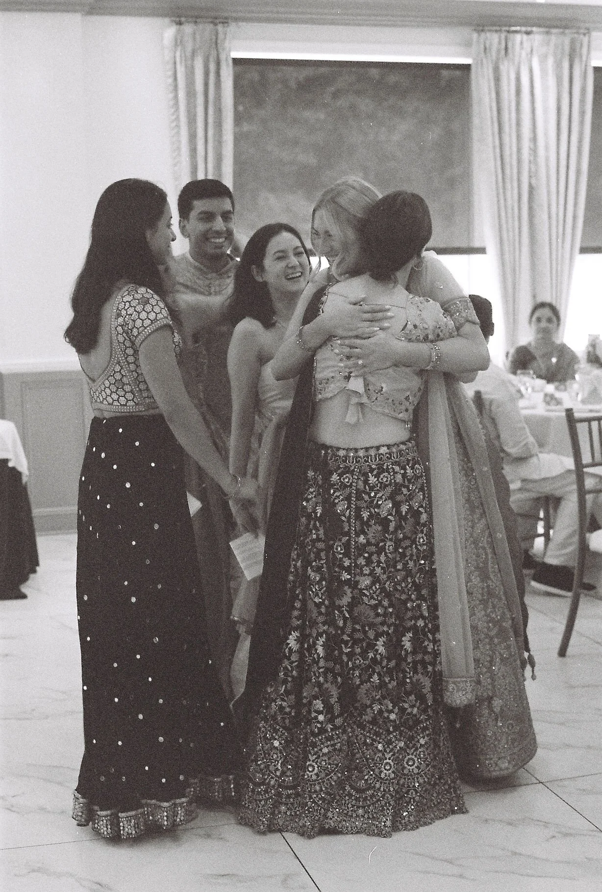 Group of women and men in traditional Indian attire sharing a joyful hug and conversation at a gathering or celebration.