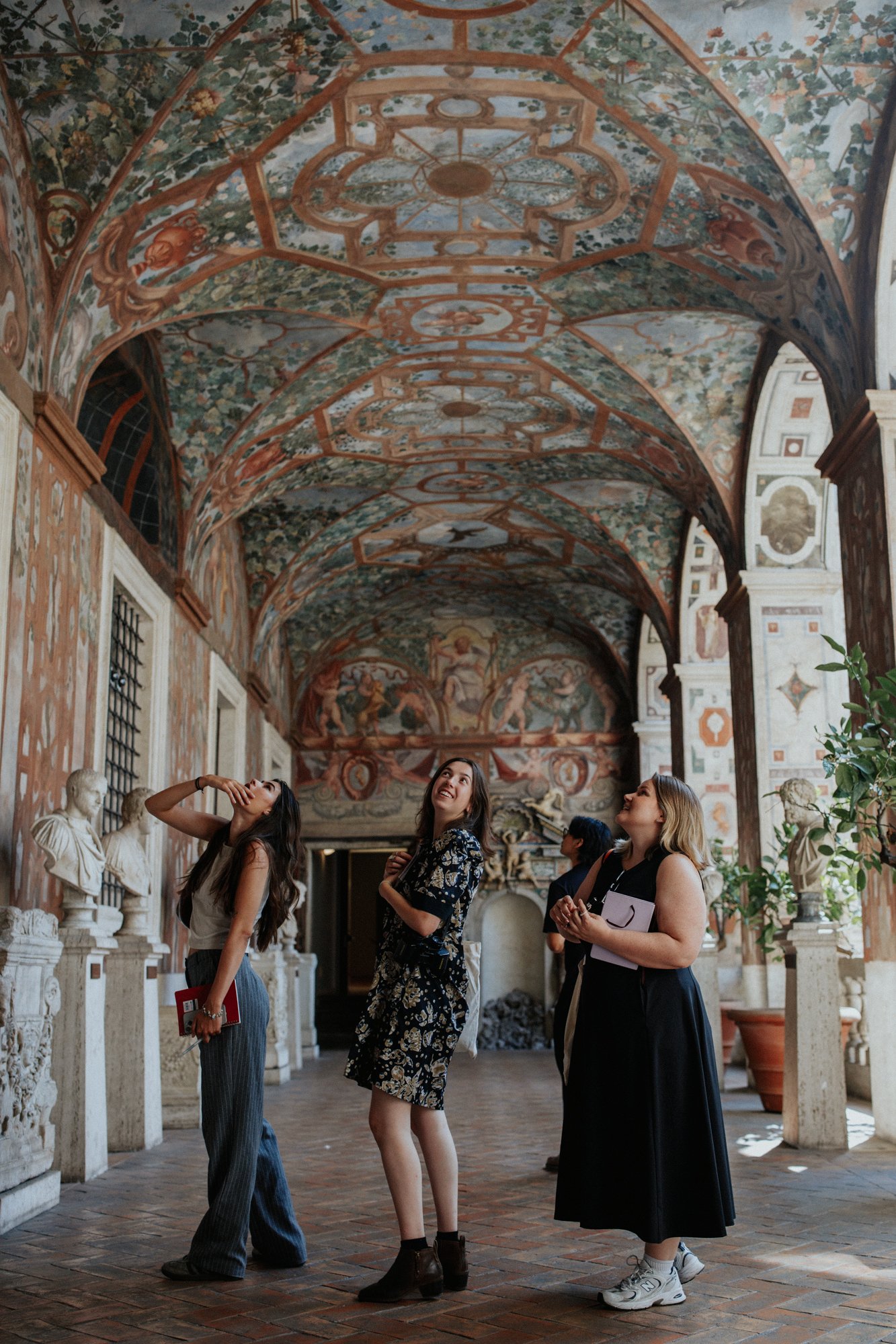 Group of women exploring a historic museum with decorated vaulted ceiling, classical statues, and ornate walls.