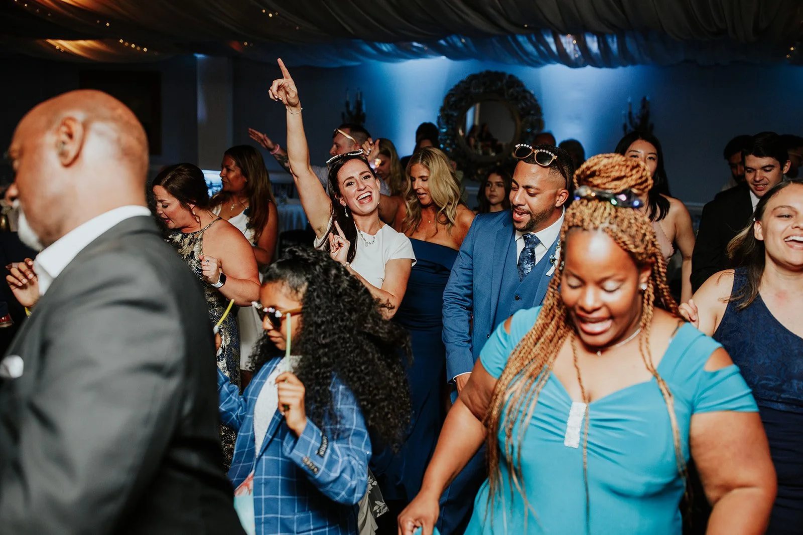 People dancing and celebrating at a lively party or wedding reception, with a woman in white raising her arm and smiling.