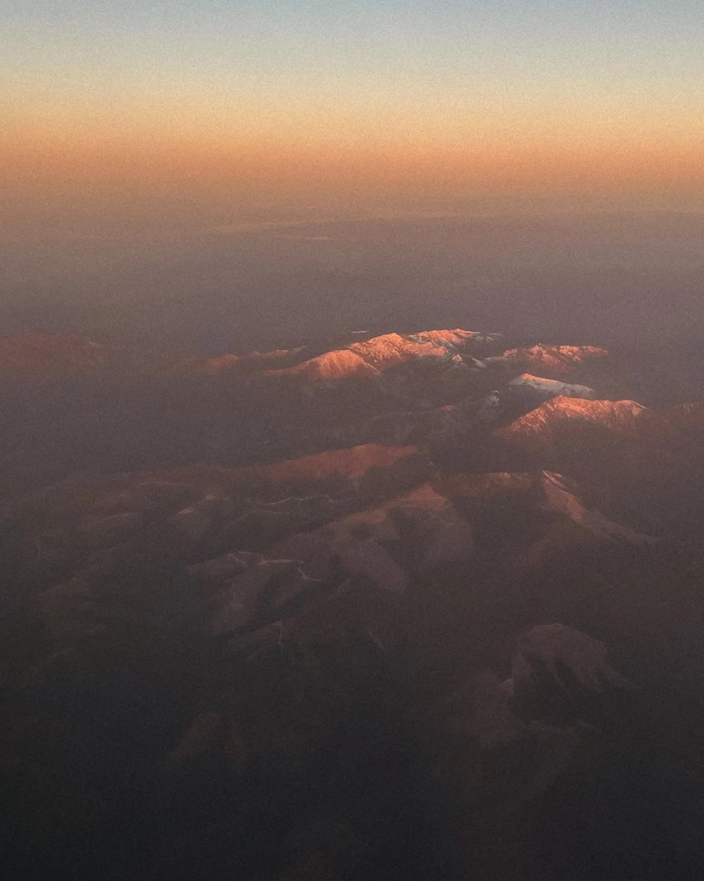 Aerial view of snow-capped mountain peaks at sunset or sunrise with a colorful sky.