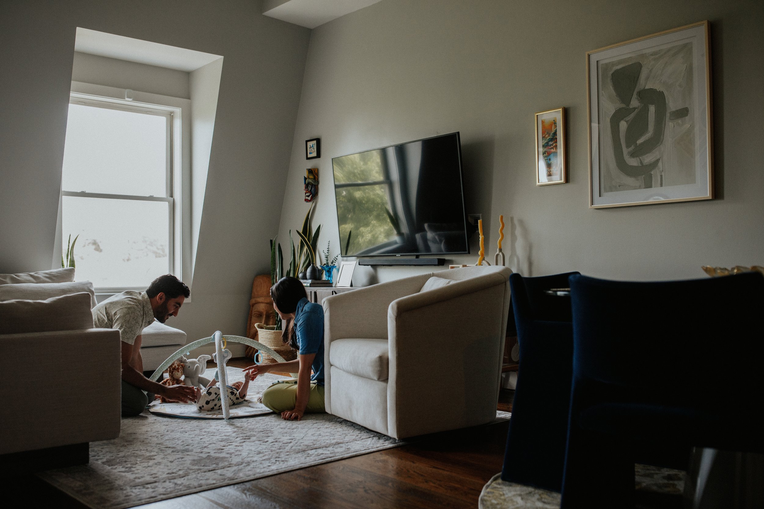 A cozy living room with a large window, a television, and family members engaging with a baby play area on the floor.
