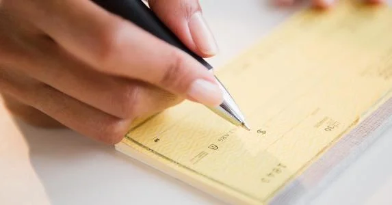 woman-writing-amount-on-yellow-check-getty_573x300.jpg