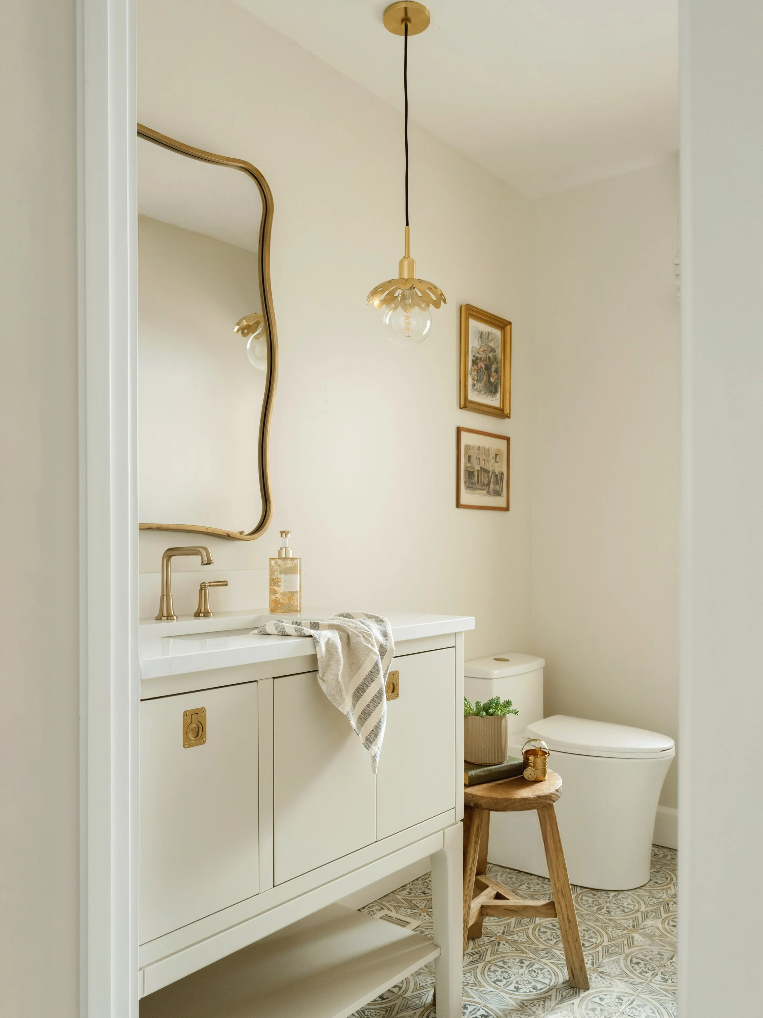 Graceful curves and carefully selected details give this powder room its distinctive character. A sculptural mirror, brass accents, and curated artwork introduce a subtle European influence, while soft neutral finishes create a space that that feels 