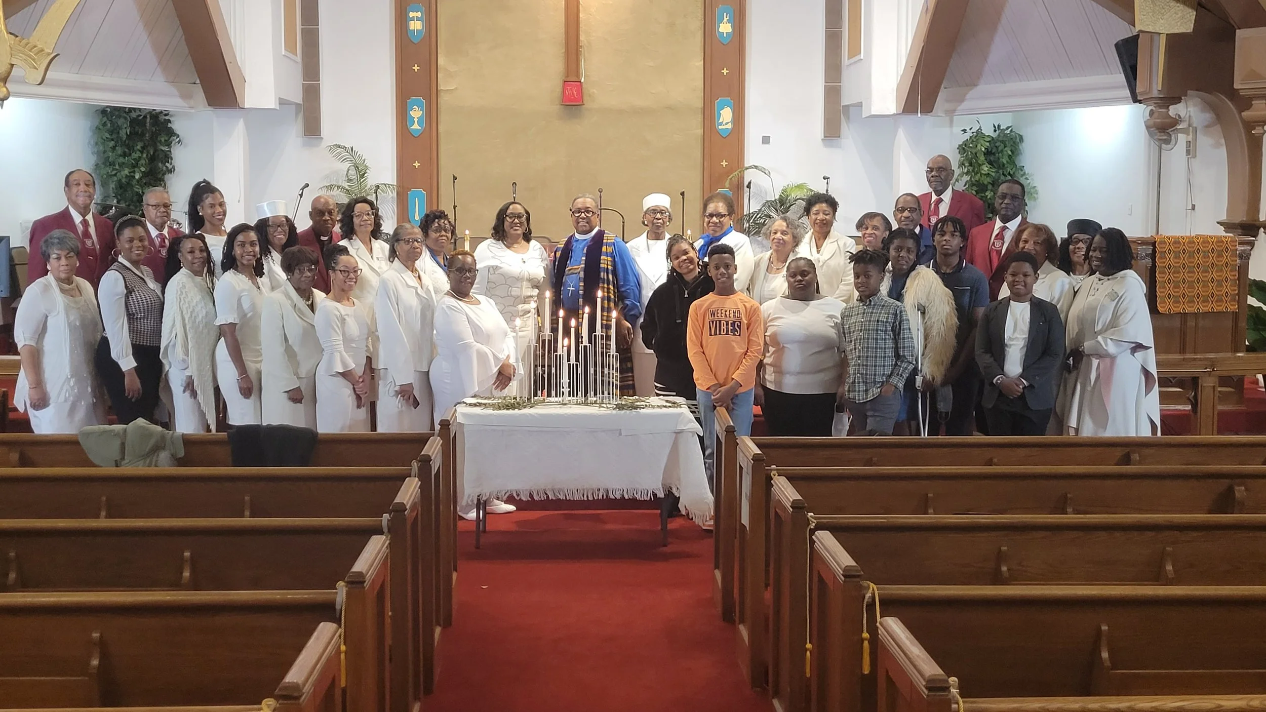 Group of people gathered inside a church celebrating a special occasion, with a table containing lit candles at the center.