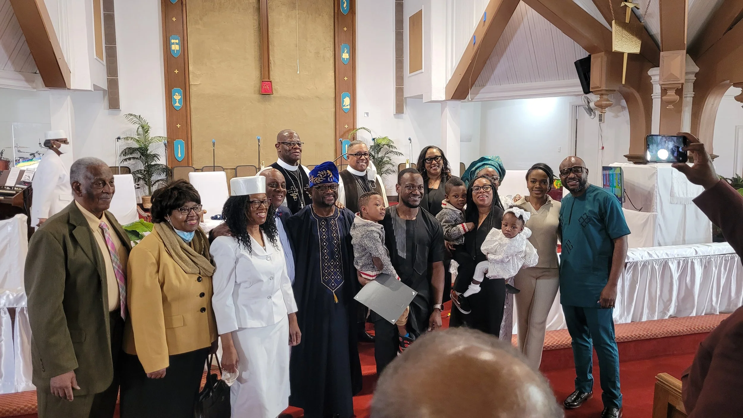 Group of diverse people, including children, gathered inside a church, posing for a photo during a special event, with a church altar and decorations in the background.