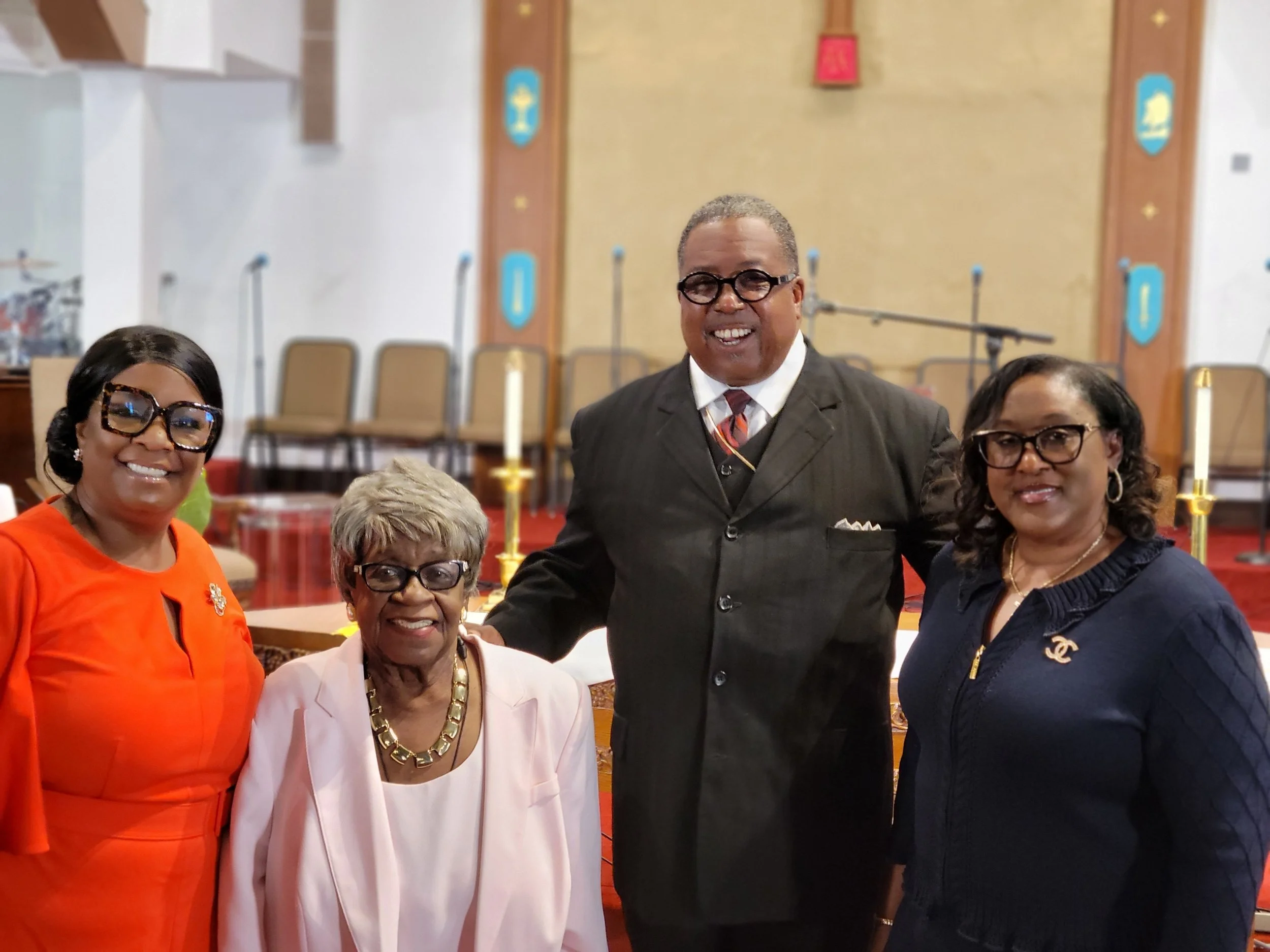 Group of four African American people standing together indoors, smiling, in a church or religious setting.