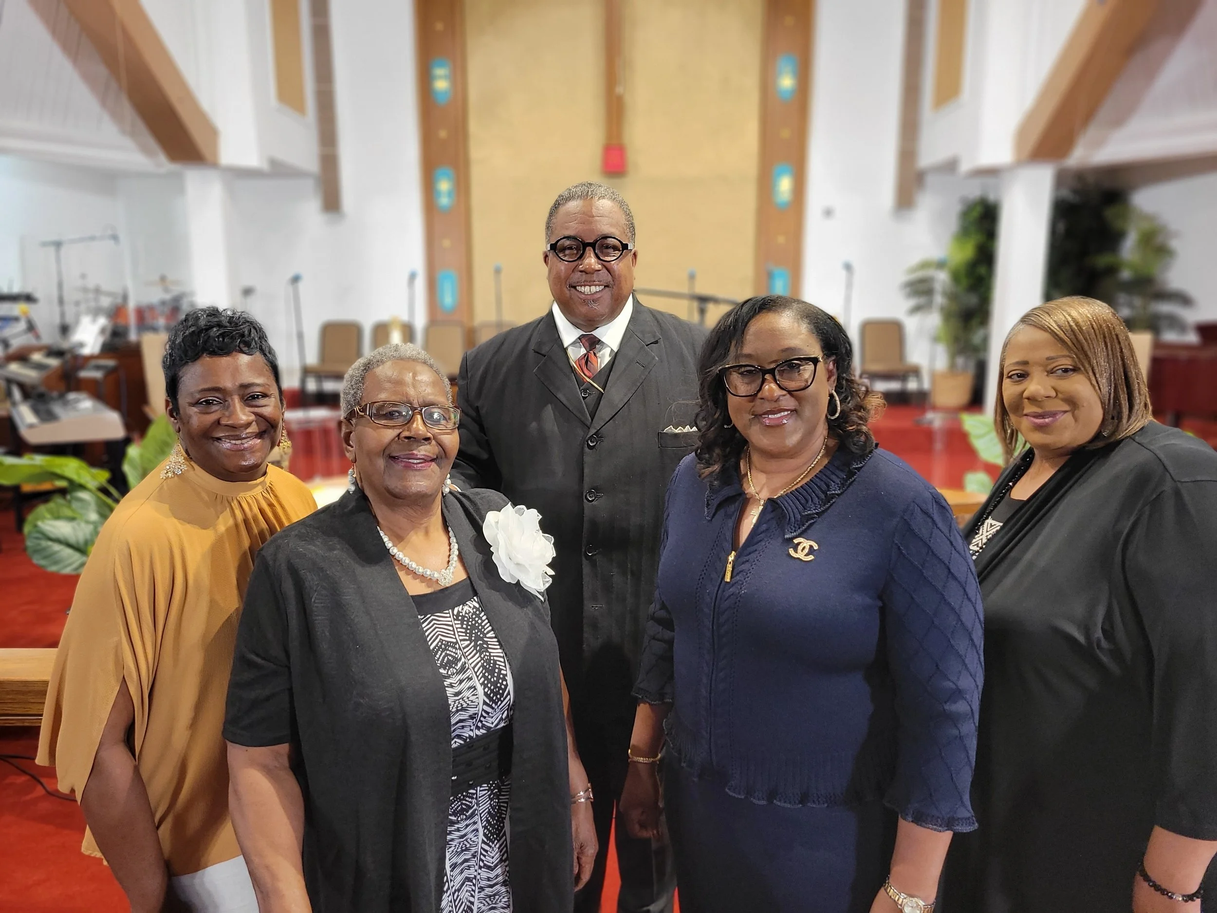 A group of six diverse people posing inside a church, smiling, dressed in formal attire.