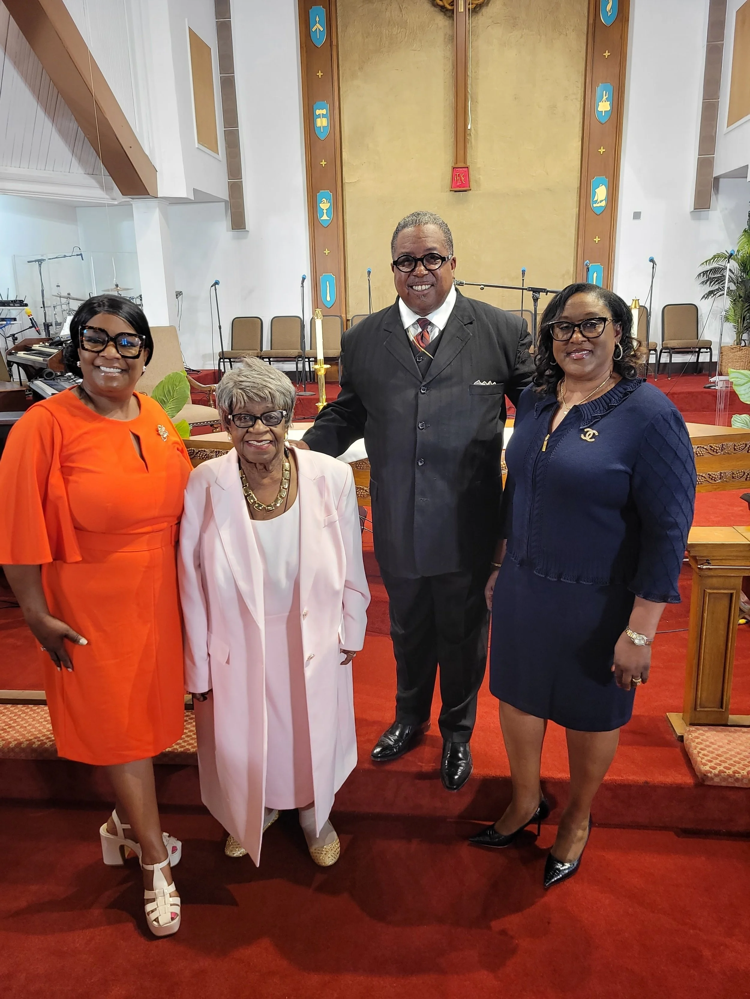 Four well-dressed individuals standing together inside a church, posing for a photo.