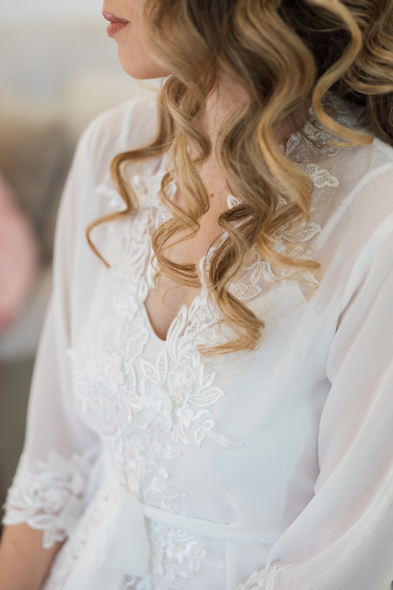 womans hair falls in ringlets onto her shoulders clothed in white lacey dress