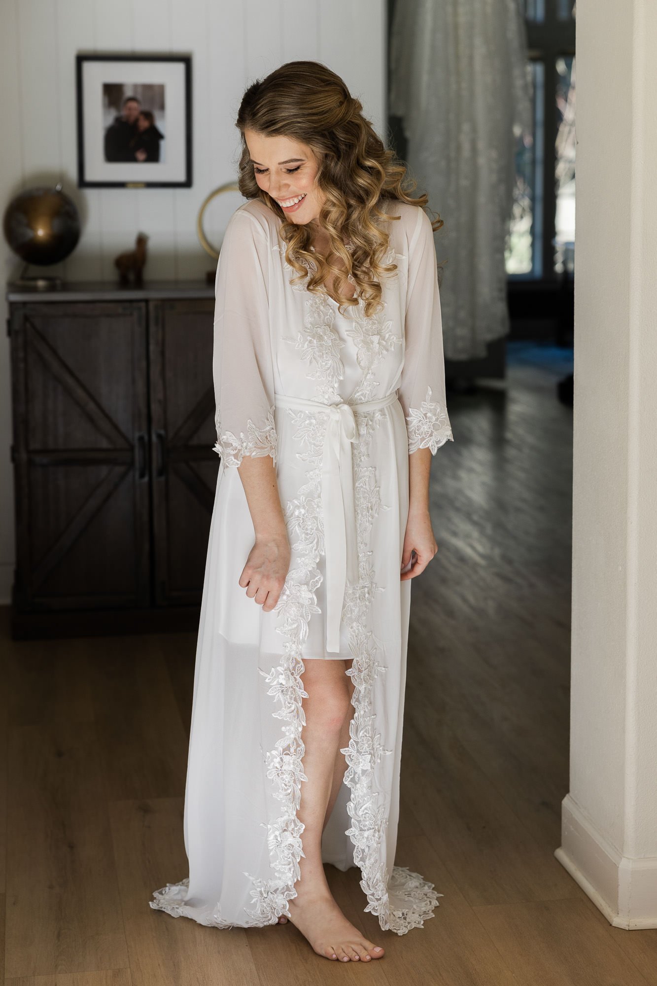 woman in white lacy robe smiles while looking down at floor