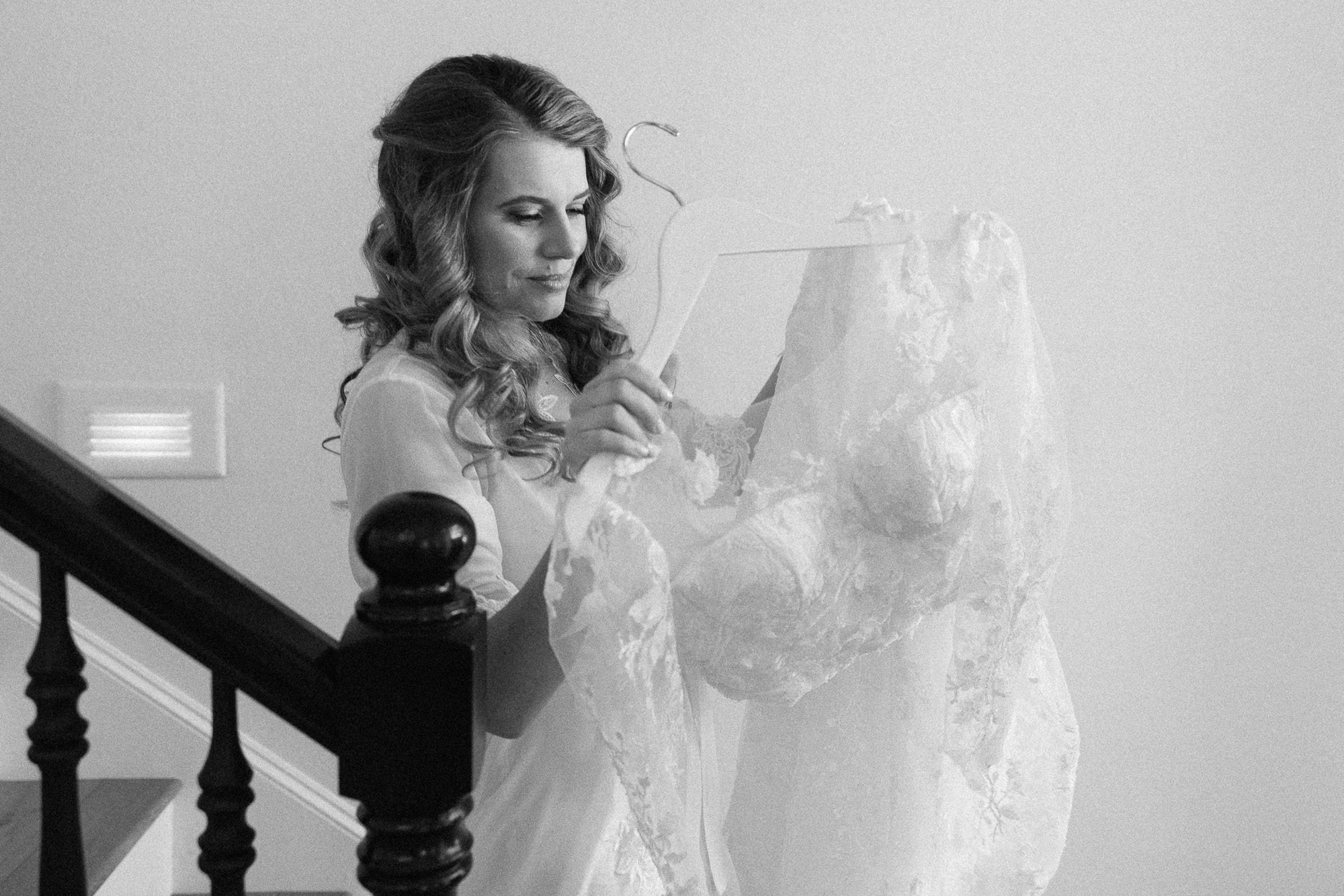 woman with curly hair carries a wedding dress on a hanger