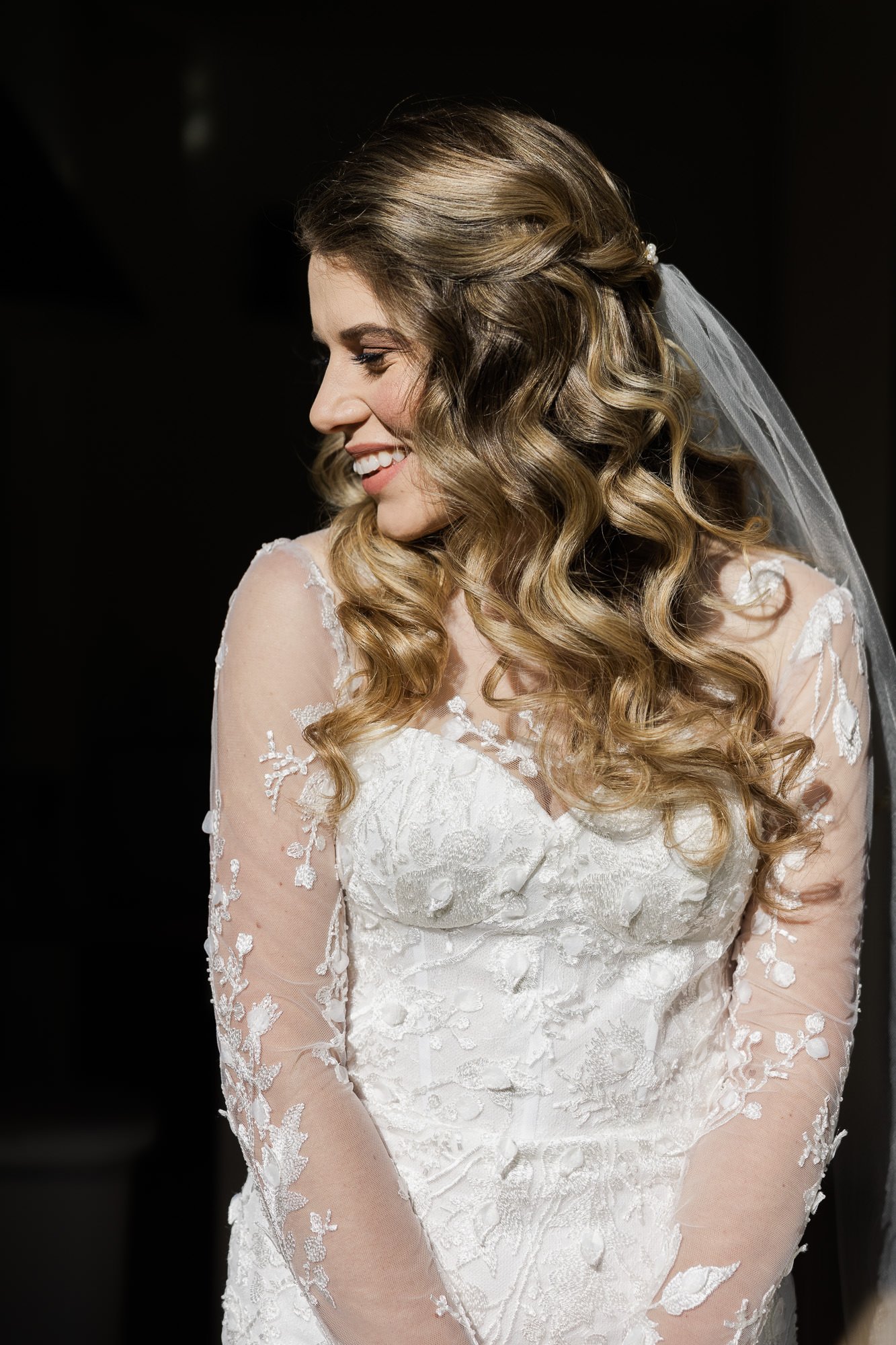 bride in wedding dress and veil looks over shoulder and smiles