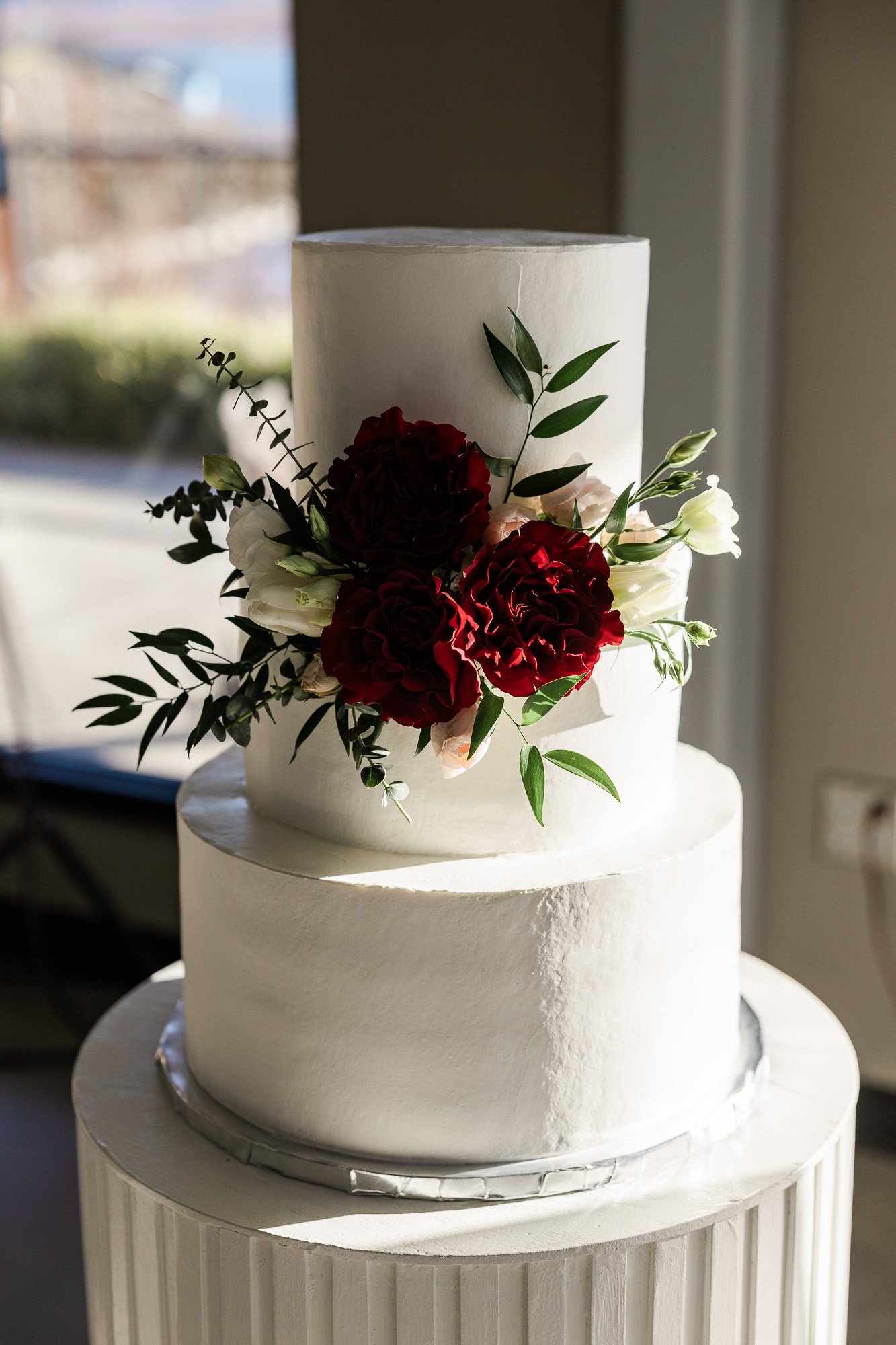 three tiered white wedding cake with red roses and greenery decor