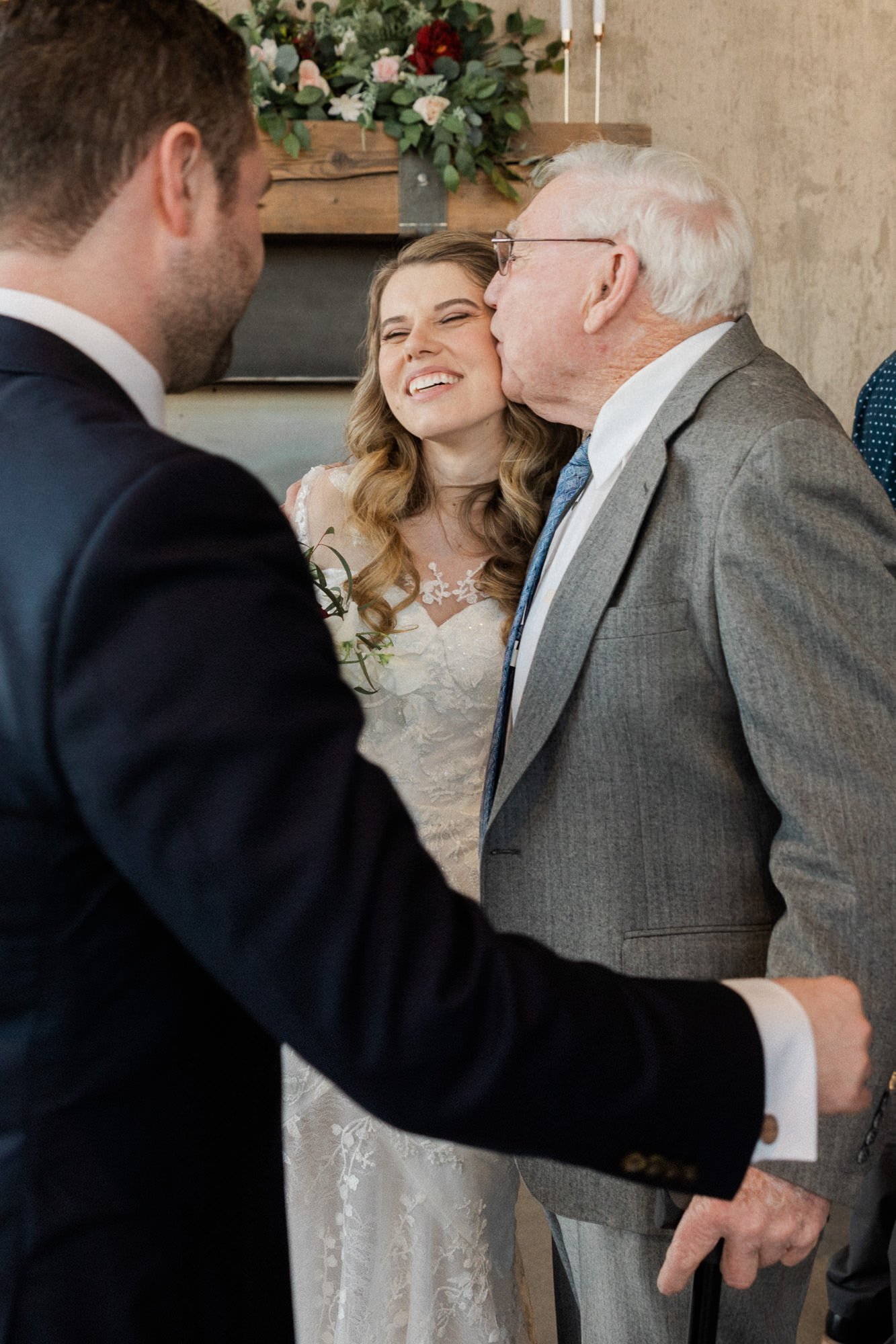 old man in gray suit kisses woman in white dress on the cheek