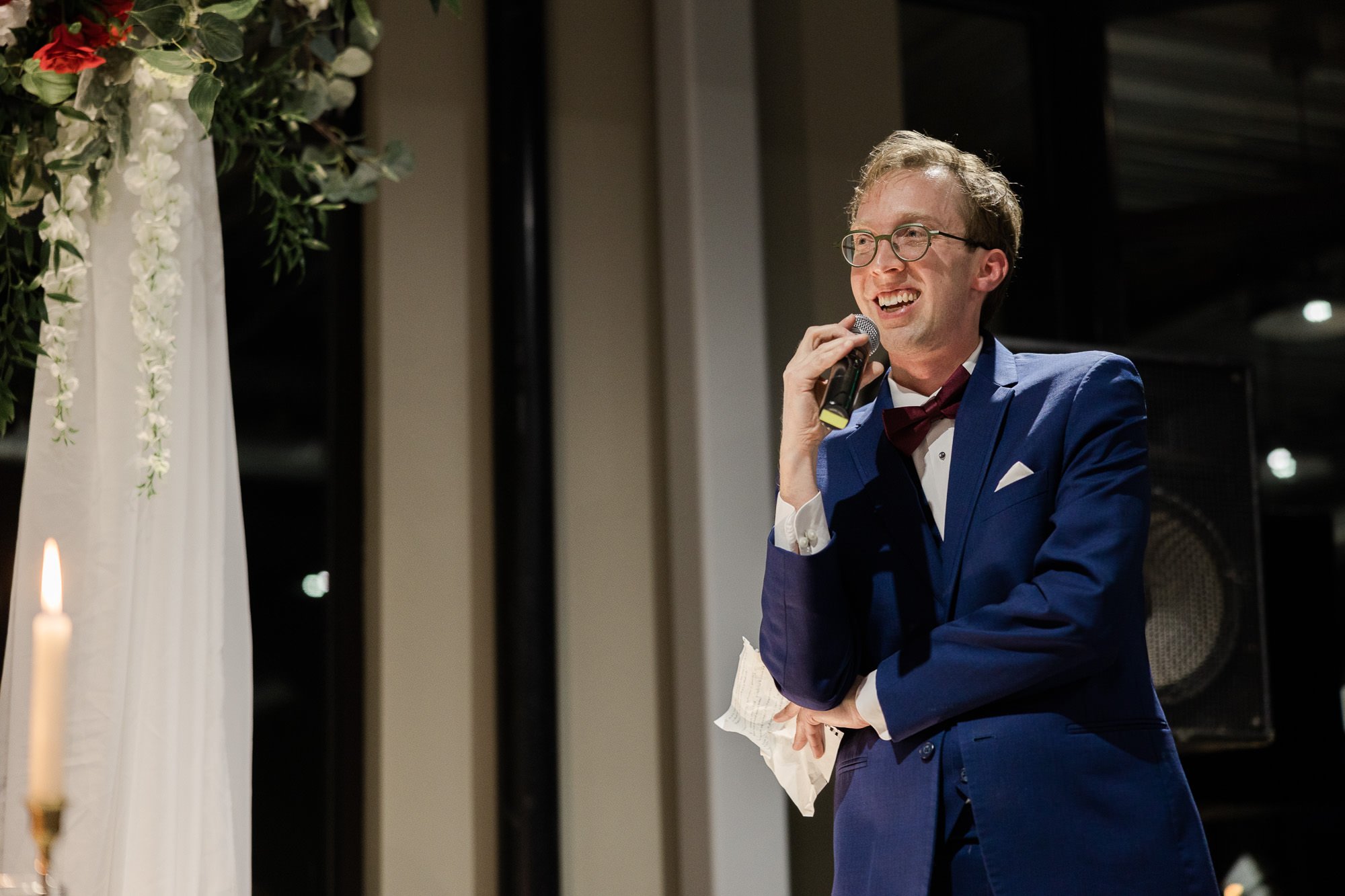 man in blue suit holds piece of paper while speaking into microphone during wedding toast