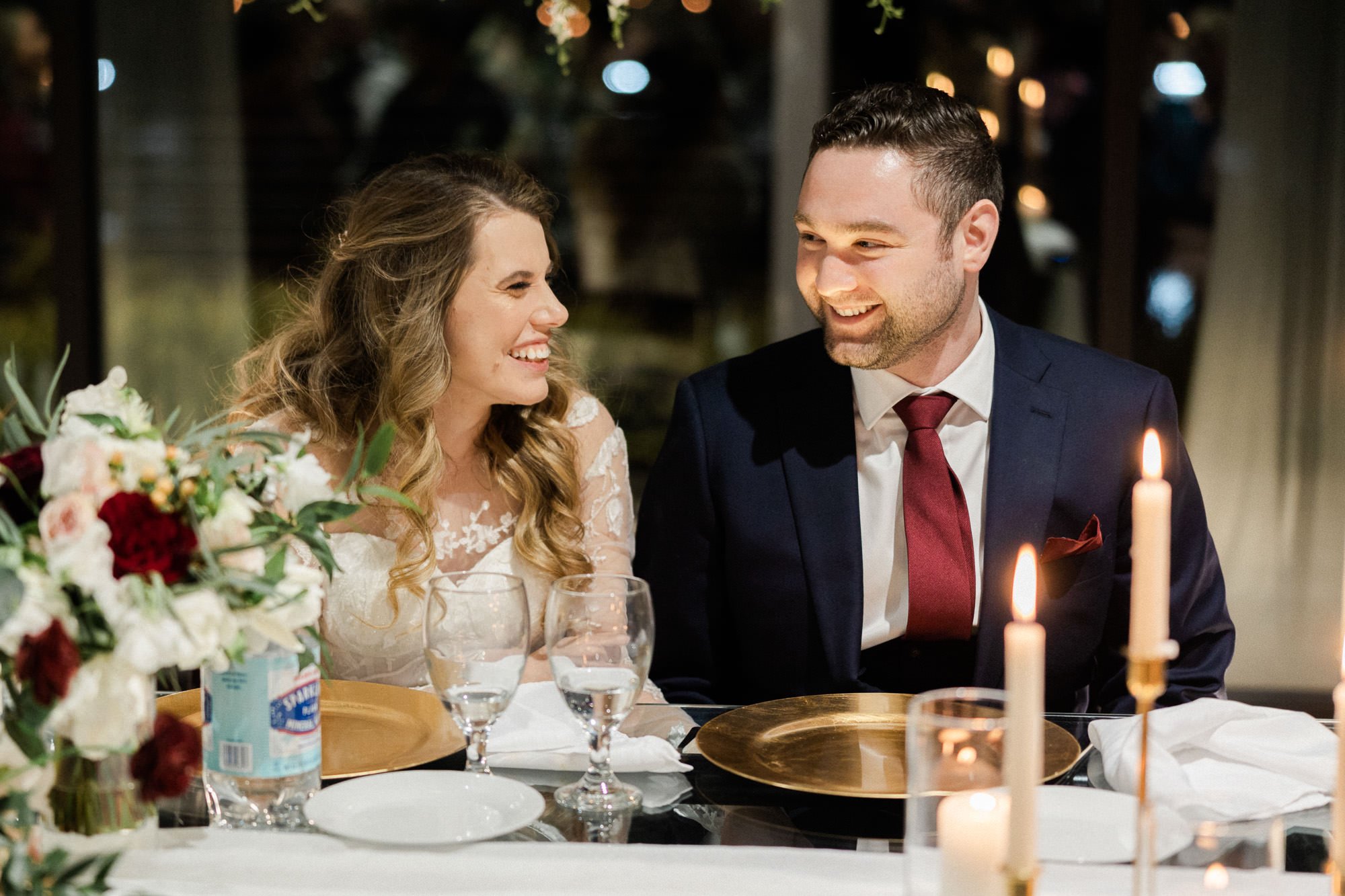 bride and groom sit at dinner table and look at each other during wedding toasts