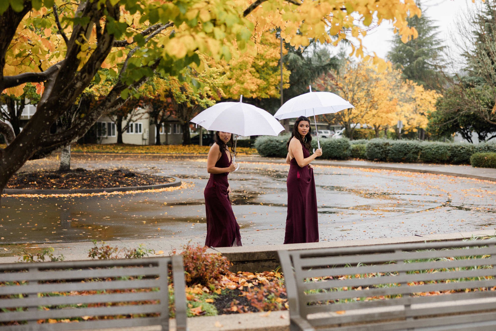 two women in burgundy bridesmaids dresses walk in lake oswego park surrounded by yellow leaves