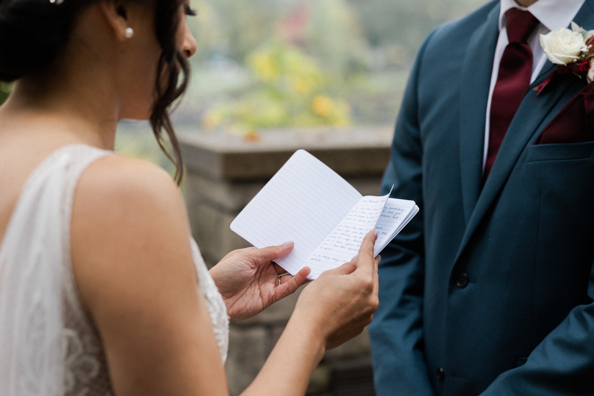 brides hands hold vow book while facing groom in blue suit