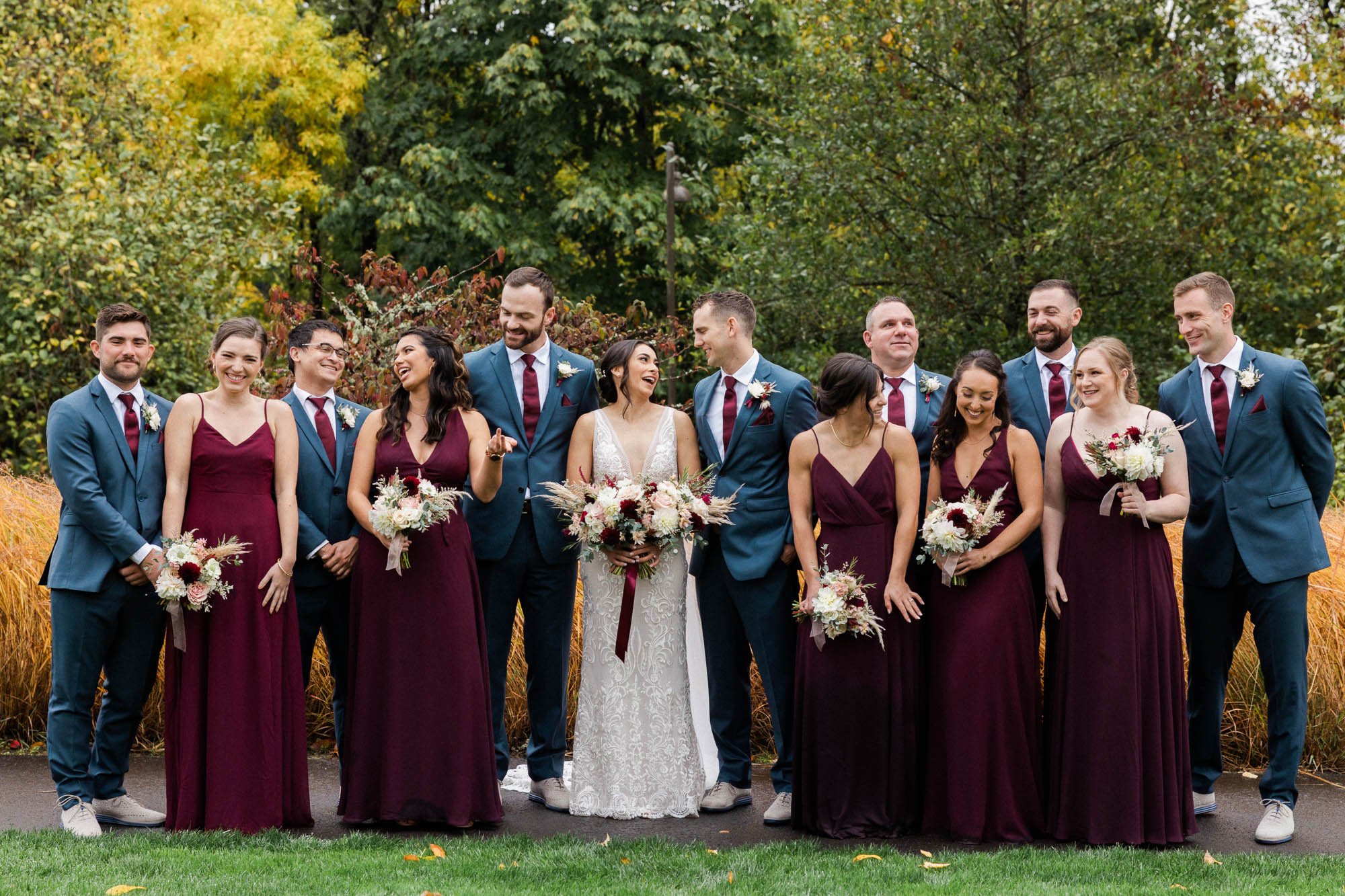 five bridesmaids in burgundy dresses and six groomsmen in navy suits stand with bride and groom in lake oswego park