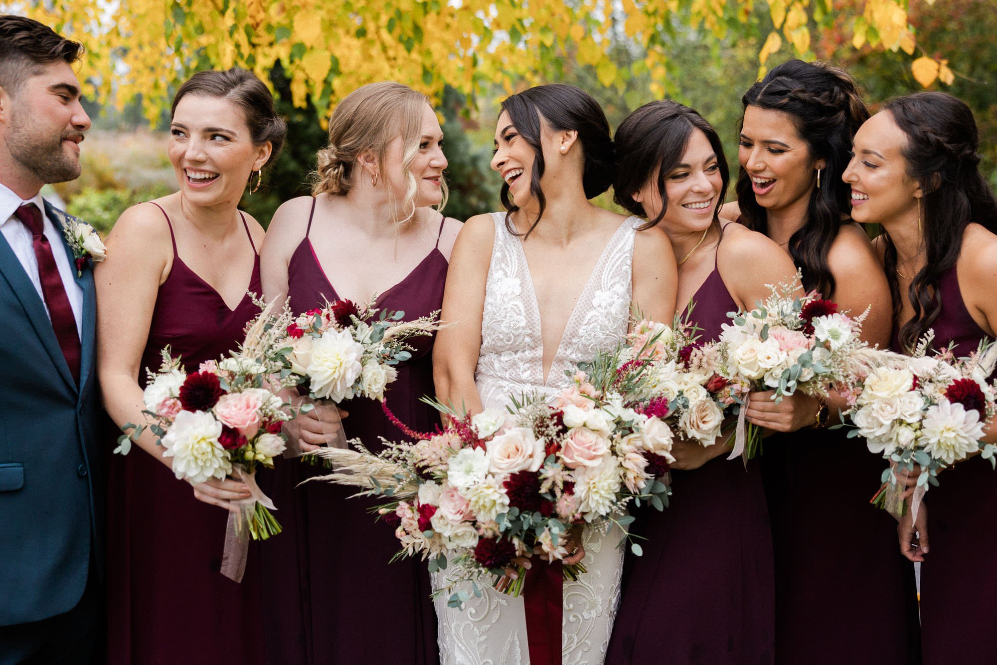 bride and six bridesmaids holding floral bouquets look at and smile at one another