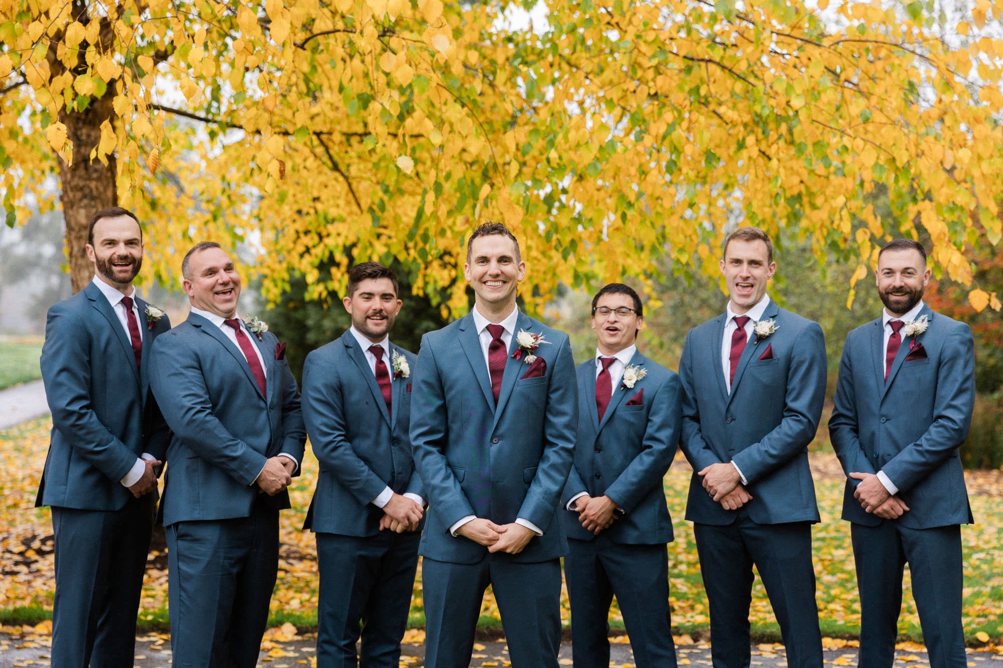 six groomsmen stand with groom under yellow leaves at lake oswego park