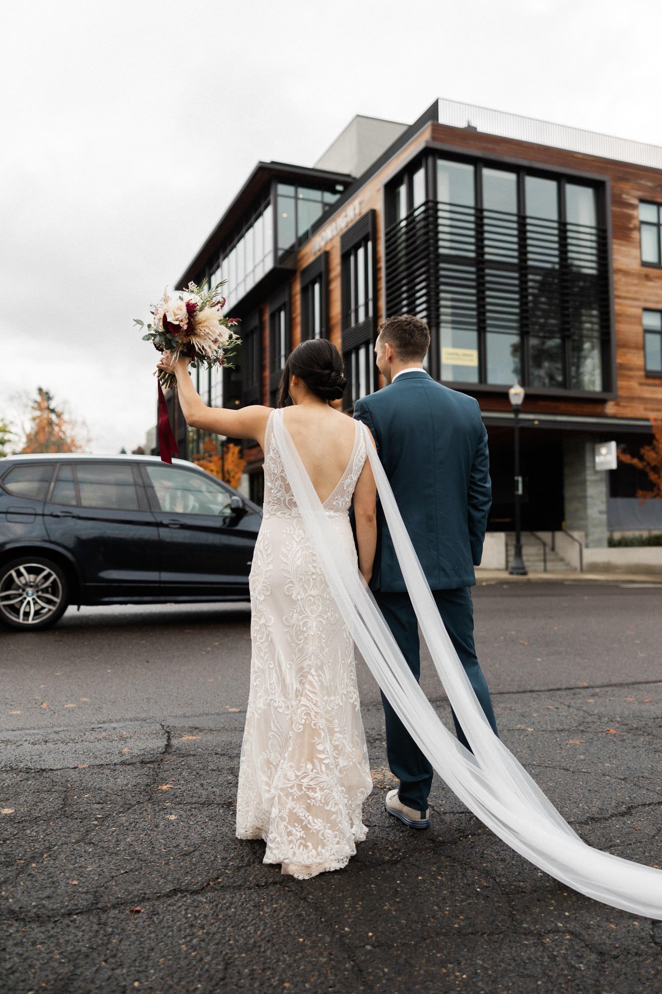 bride in white gown and long train and groom in navy suit walk toward ironlight wedding venue in lake oswego, oregon