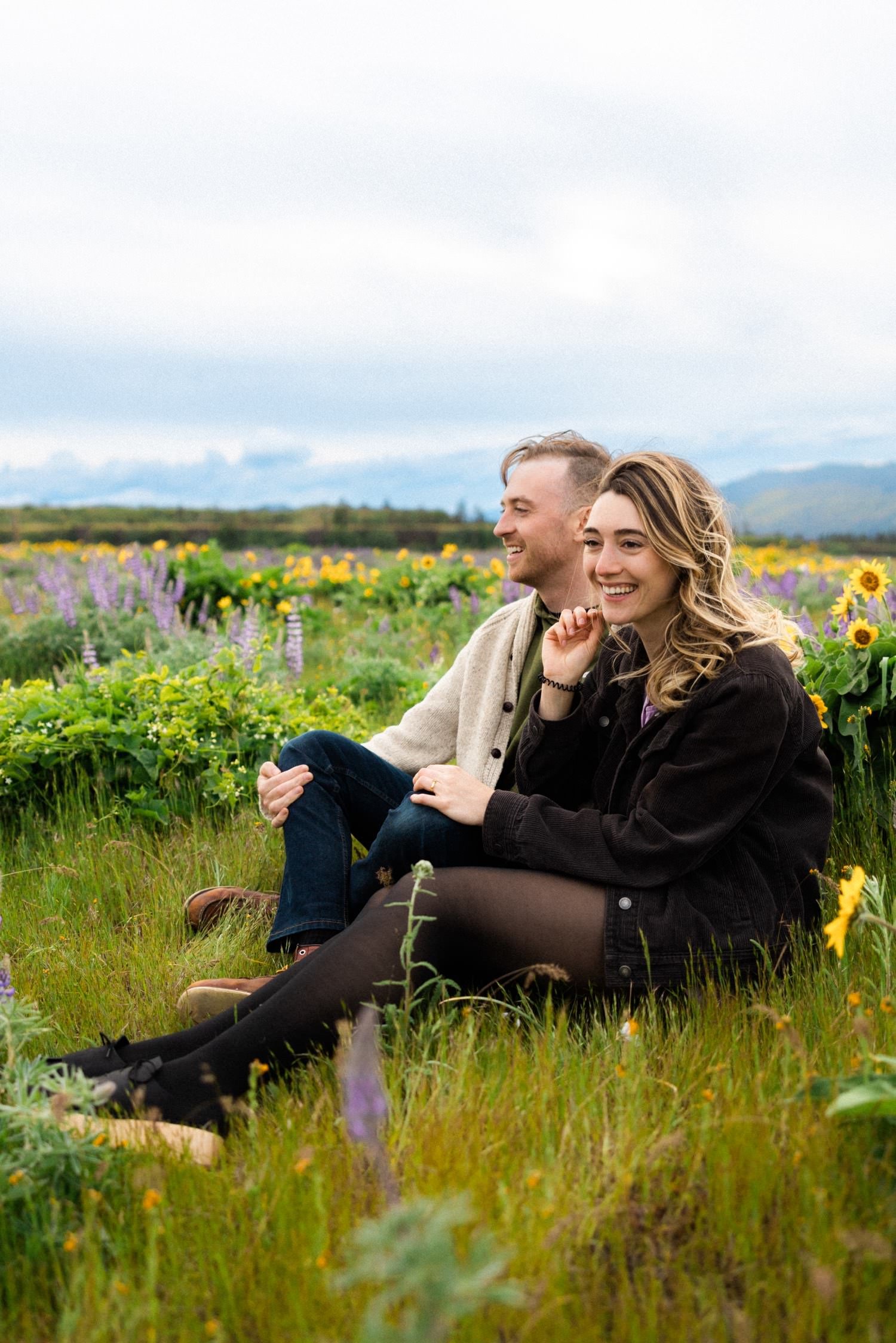 02_Wildflower Engagement Session at Rowena Crest48_man and woman sit next to each other and smile in field of wild flowers.jpg