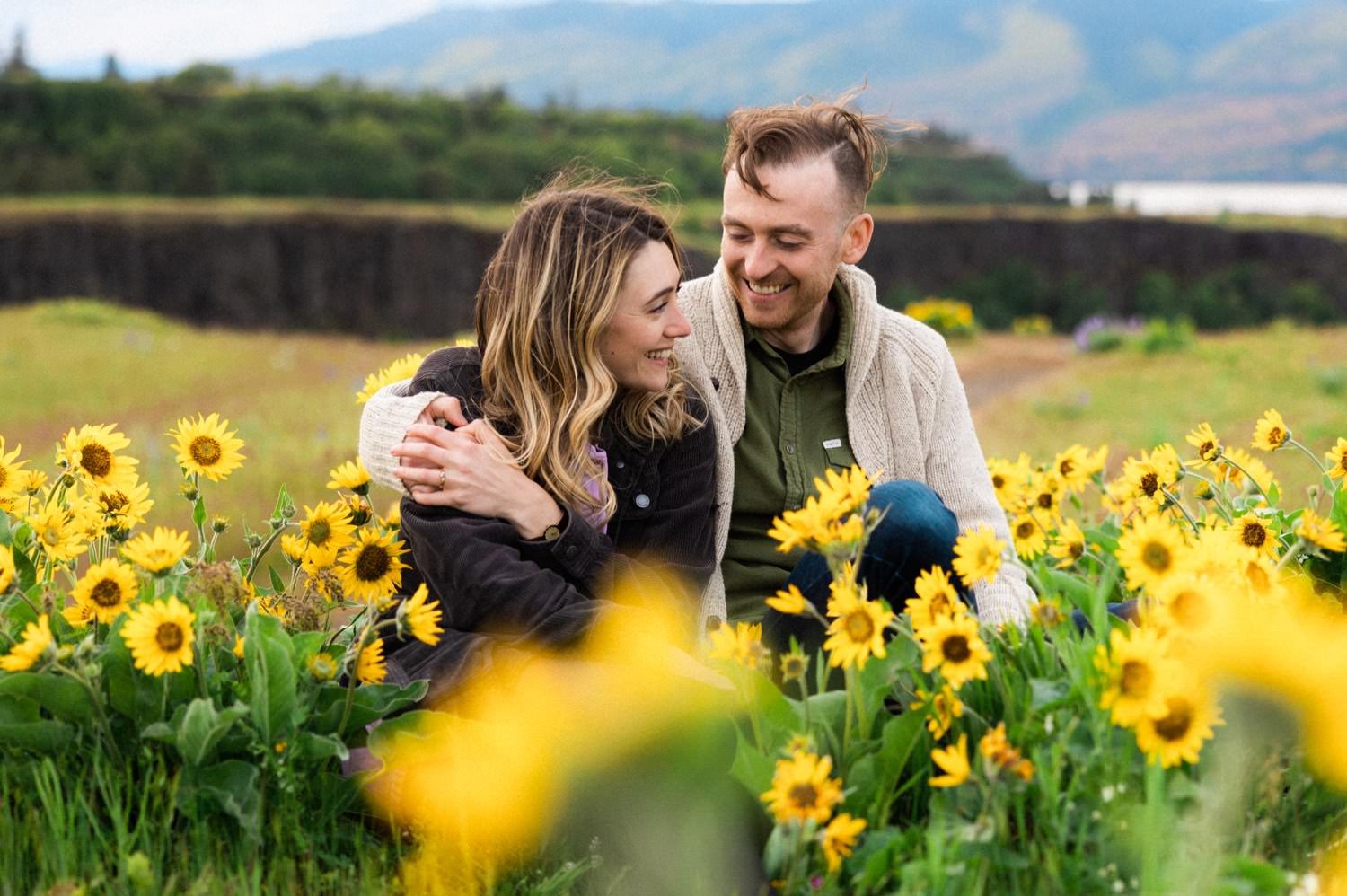 16_Wildflower Engagement Session at Rowena Crest78_man and woman sit next to each other in field of wildflowers during engagement shoot at rowena crest.jpg